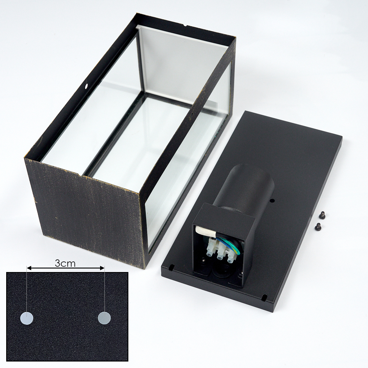 Eine offene, rechteckige Lampe aus Schwarz und Glas, zerlegt. Die Basis ist separat. Daneben ein 3 cm langes Lineal.
