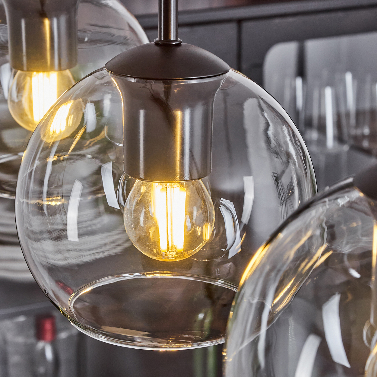 Nahaufnahme von drei modernen Glaspendelleuchten. Jede hat einen runden Glasschirm mit einer sichtbaren, leuchtenden Glühbirne.