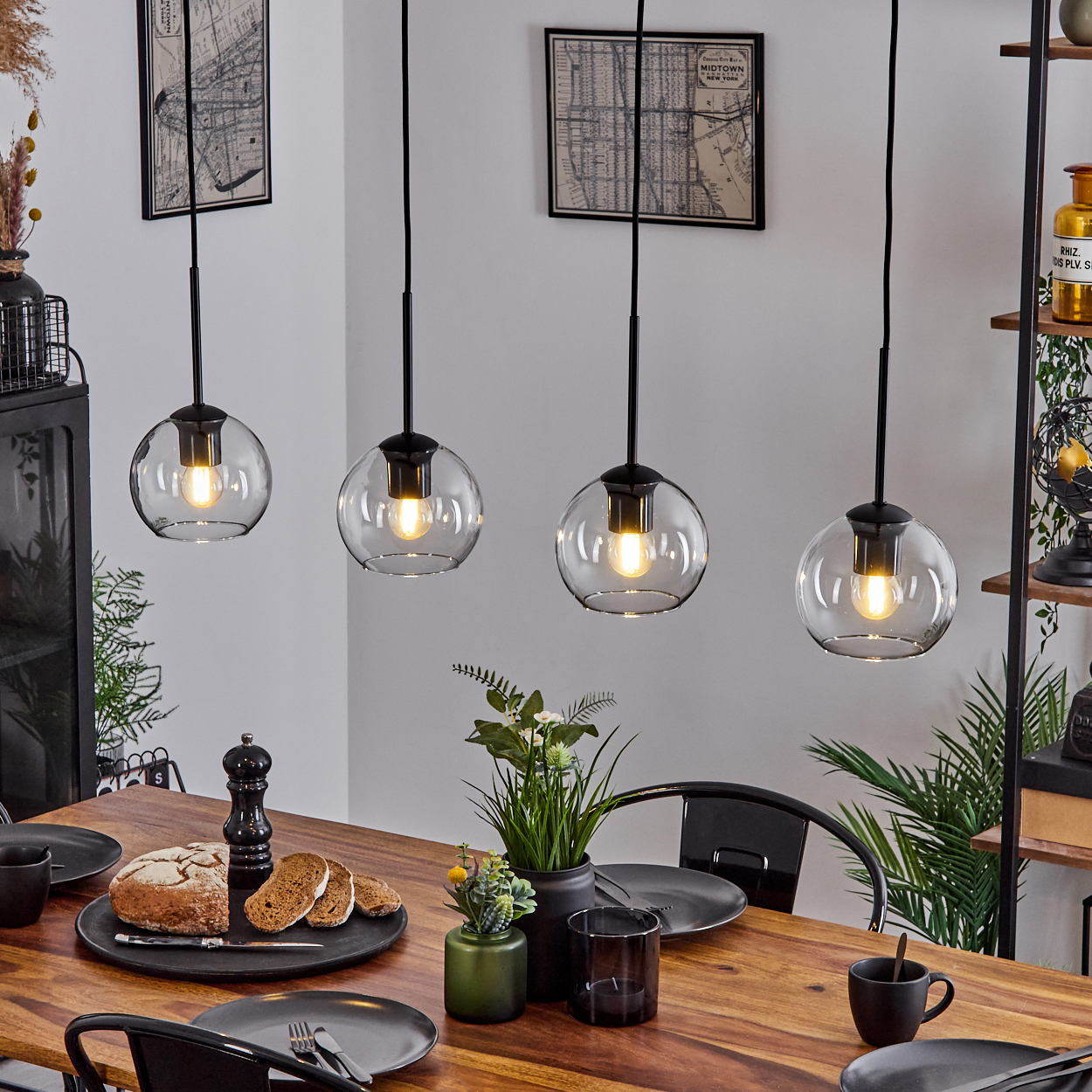 Esszimmertisch mit Brot, Tellern und Blumen. Vier hängende Kugelleuchten beleuchten die Szene, Karten an der Wand.
