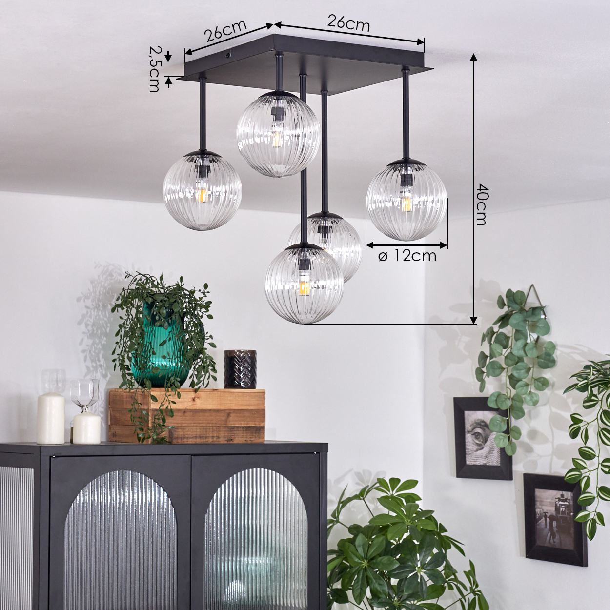 Eine moderne Deckenleuchte mit fünf gerippten Glaskugeln hängt von der Decke. Darunter sind ein Schrank und Pflanzen zu sehen.