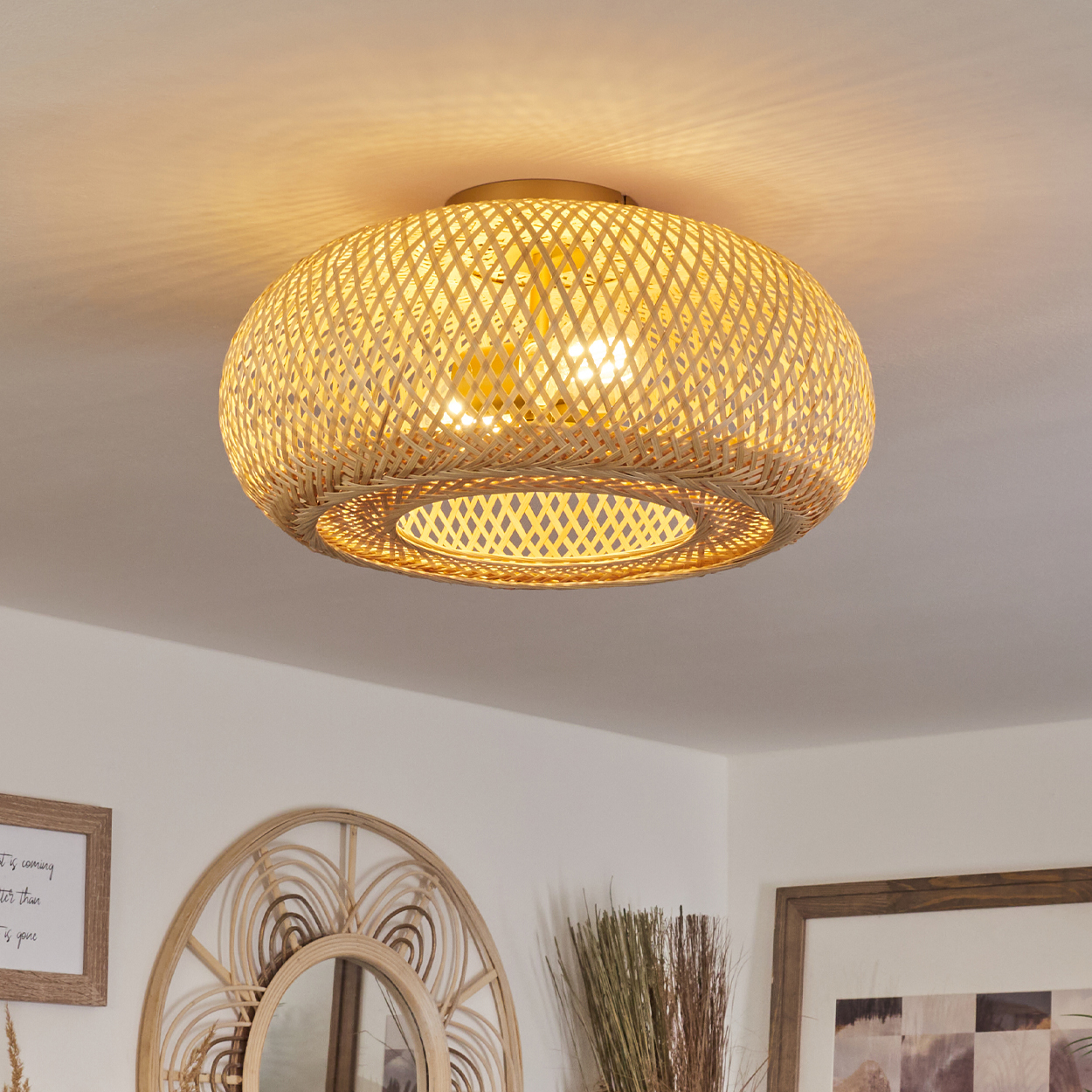 Eine gewebte Deckenlampe aus Rattan beleuchtet einen Raum. Darunter sind ein Spiegel, gerahmte Kunst und Dekorationsartikel zu sehen.