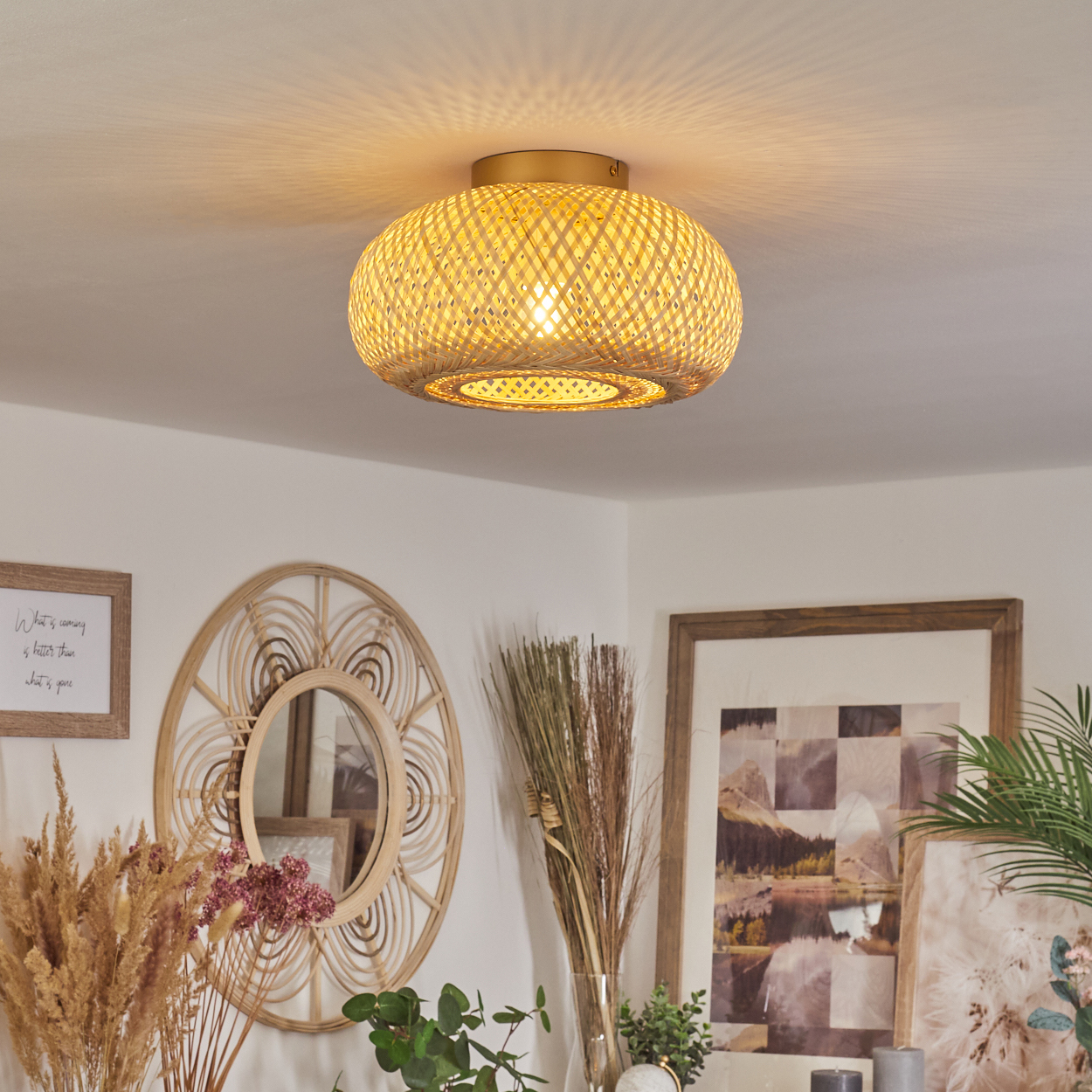 Eine Deckenlampe aus geflochtenem Rattan beleuchtet einen Raum mit warmem Schein. Dekorative Gegenstände wie Spiegel und Pflanzen sind sichtbar.