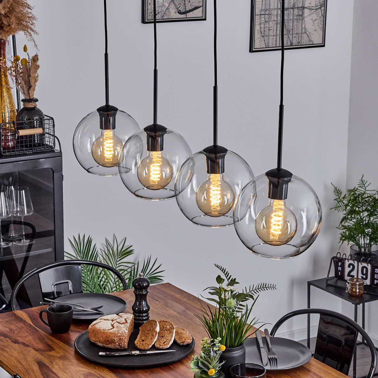 Esstisch mit Brot, Tellern und hängenden Kugelleuchten. Pflanzen und Dekorationen im Hintergrund. Ein modernes Interieur.