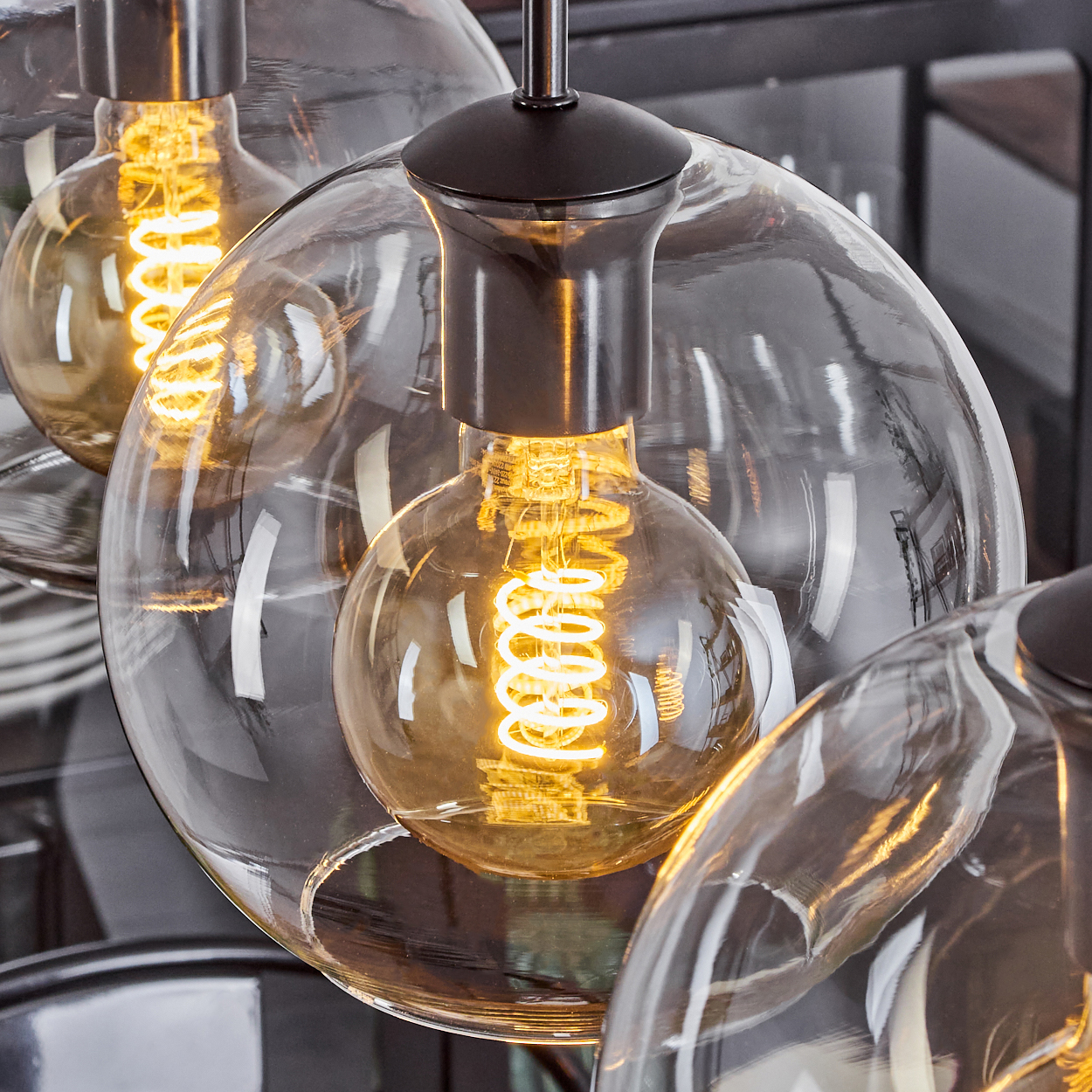 Nahaufnahme moderner Leuchten. Jede hat eine klare Glaskugel, die eine glühende, spiralförmige Glühbirne umschließt. Dunkle Metallvorrichtungen stützen die Kugeln.