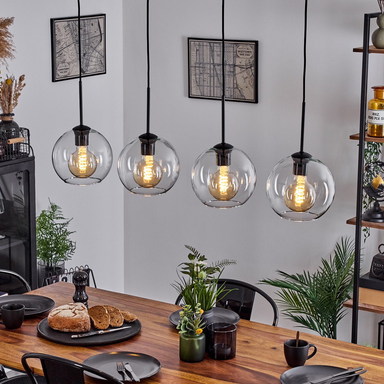 Esszimmer mit Holztisch, vier Kugellampen. Teller, Brot und Pflanzen stehen auf dem Tisch. Karten an der Wand.