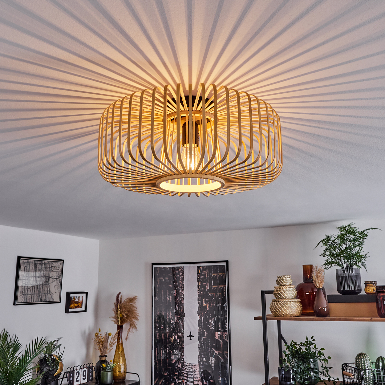 Eine Holzdeckenlampe wirft Streifenschatten. Darunter ist ein Raum mit Dekor zu sehen, darunter ein Bild von Gebäuden, Pflanzen und Regalen.