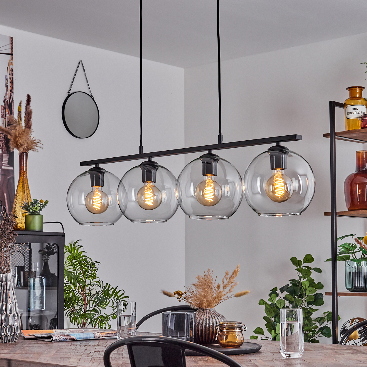 Esszimmer mit Holztisch, schwarzen Stühlen und einer Hängelampe mit vier Glaskugeln und sichtbaren Glühbirnen.