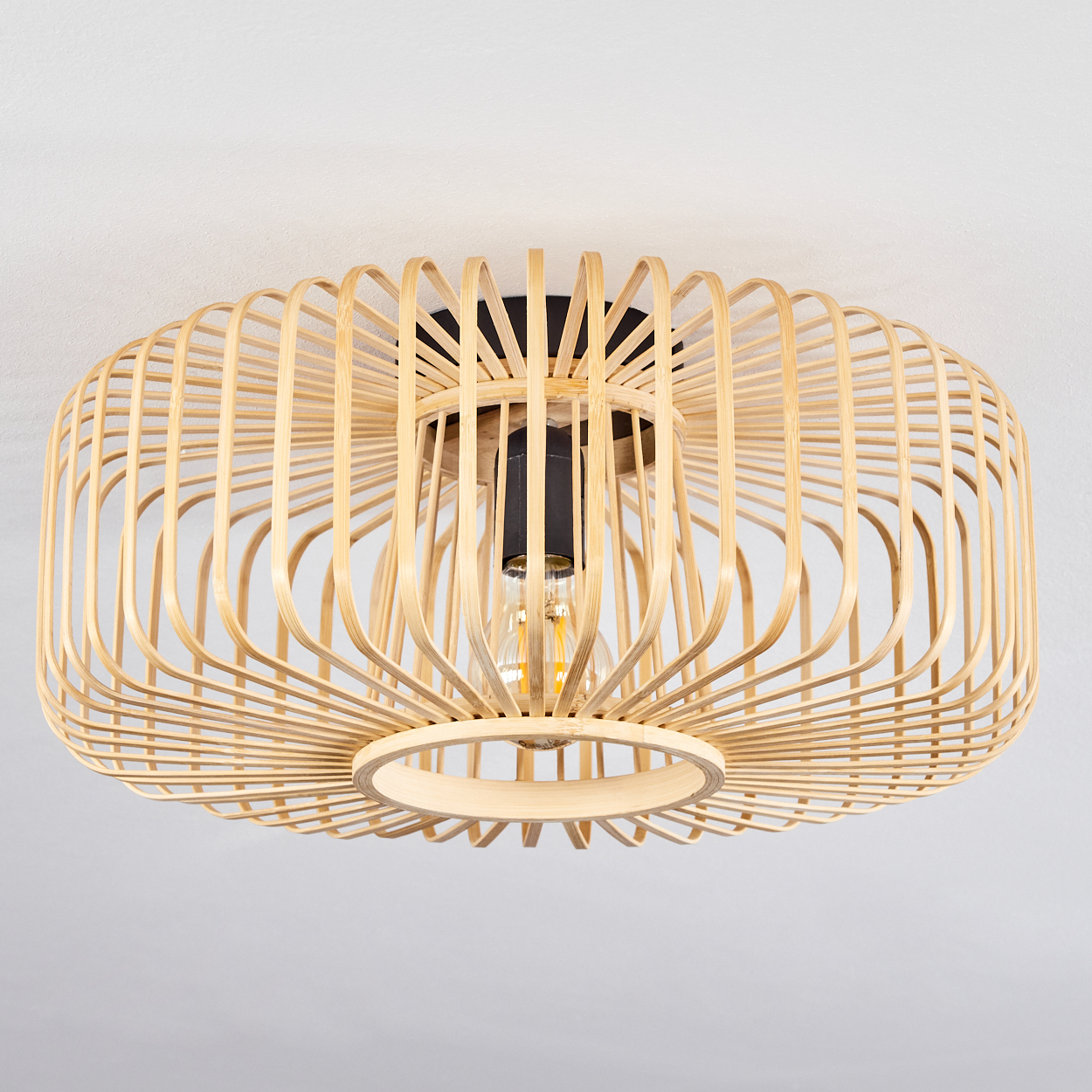 Eine Deckenlampe aus Bambus mit schwarzem Mittelteil und freiliegender Glühbirne. Der Hintergrund ist eine weiße Decke.