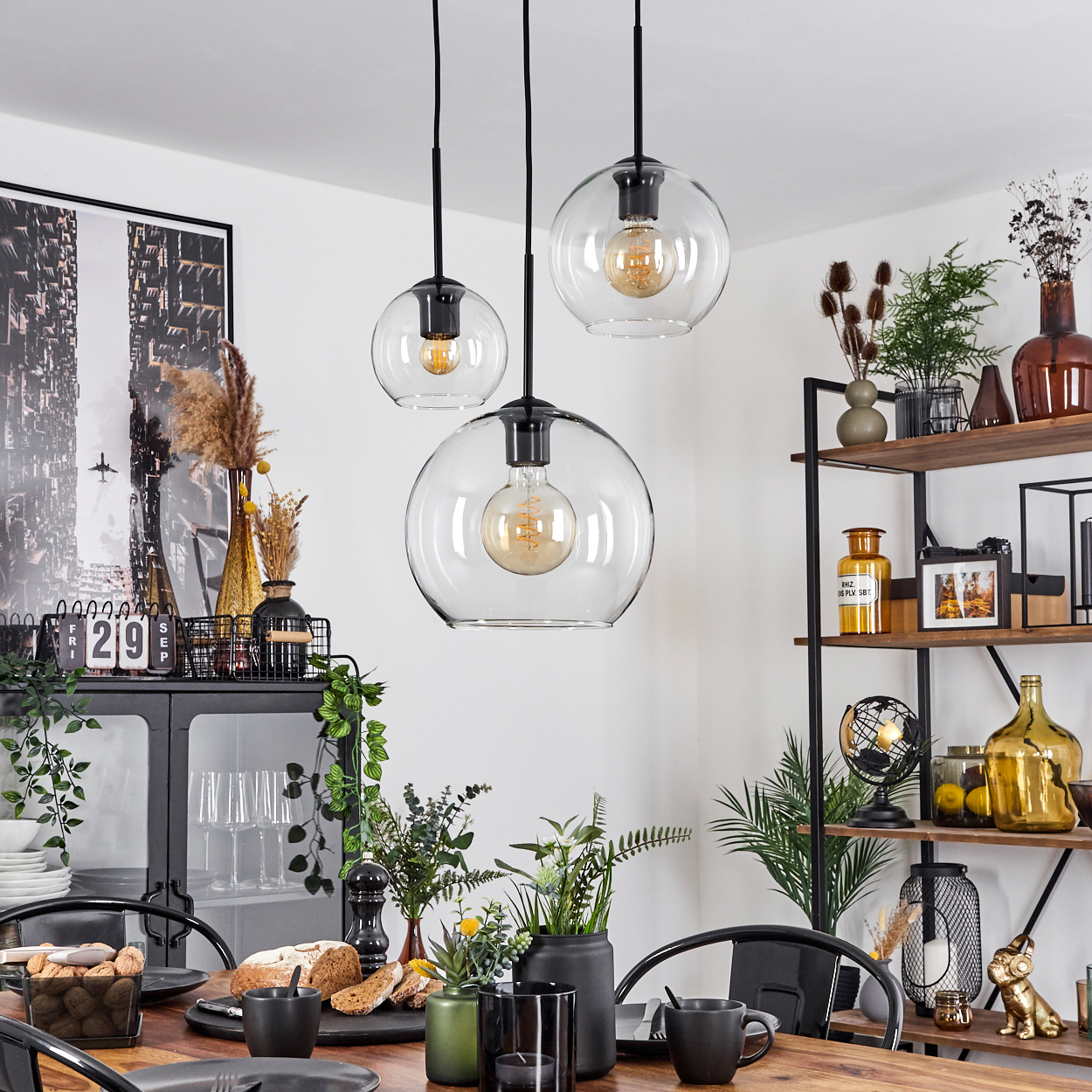 Esszimmer mit drei Kugelleuchten, Tisch mit Essen und Regalen mit Dekorationen an einer weißen Wand.
