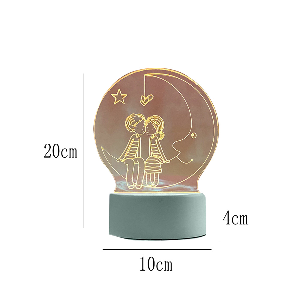 Eine dekorative Lampe mit zwei Figuren auf dem Mond. Der Sockel ist grau, mit Beschriftungen. Ein Stern und ein Herz sind ebenfalls vorhanden.