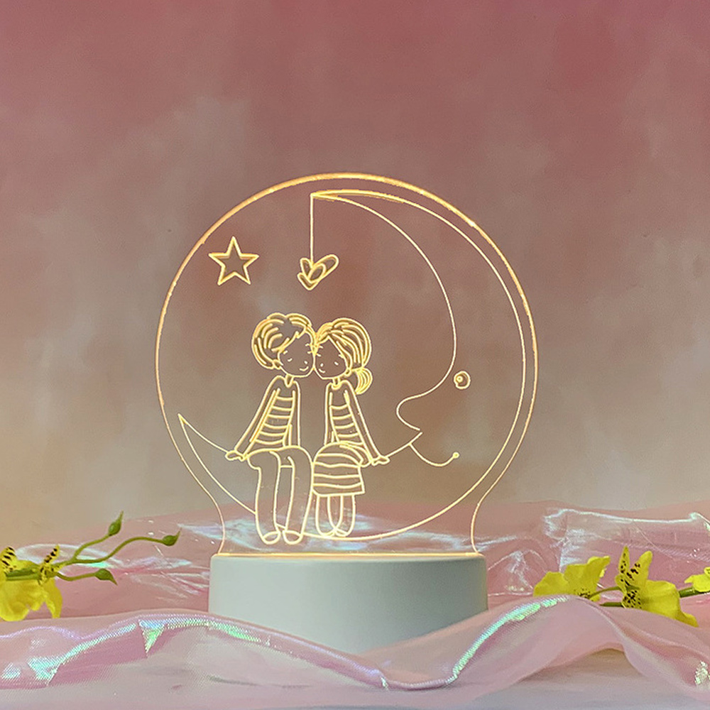 Eine leuchtende Mondlampe mit zwei sich küssenden Cartoonfiguren. Ein Stern und ein Herz hängen darüber. Rosa Hintergrund mit Blumen.