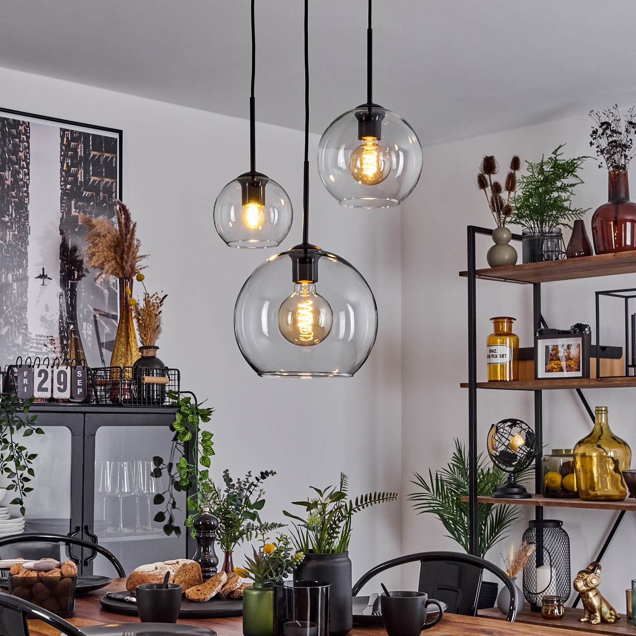 Esszimmer mit drei Hängelampen. Tisch mit Brot und Tassen gedeckt, Regal im Hintergrund.