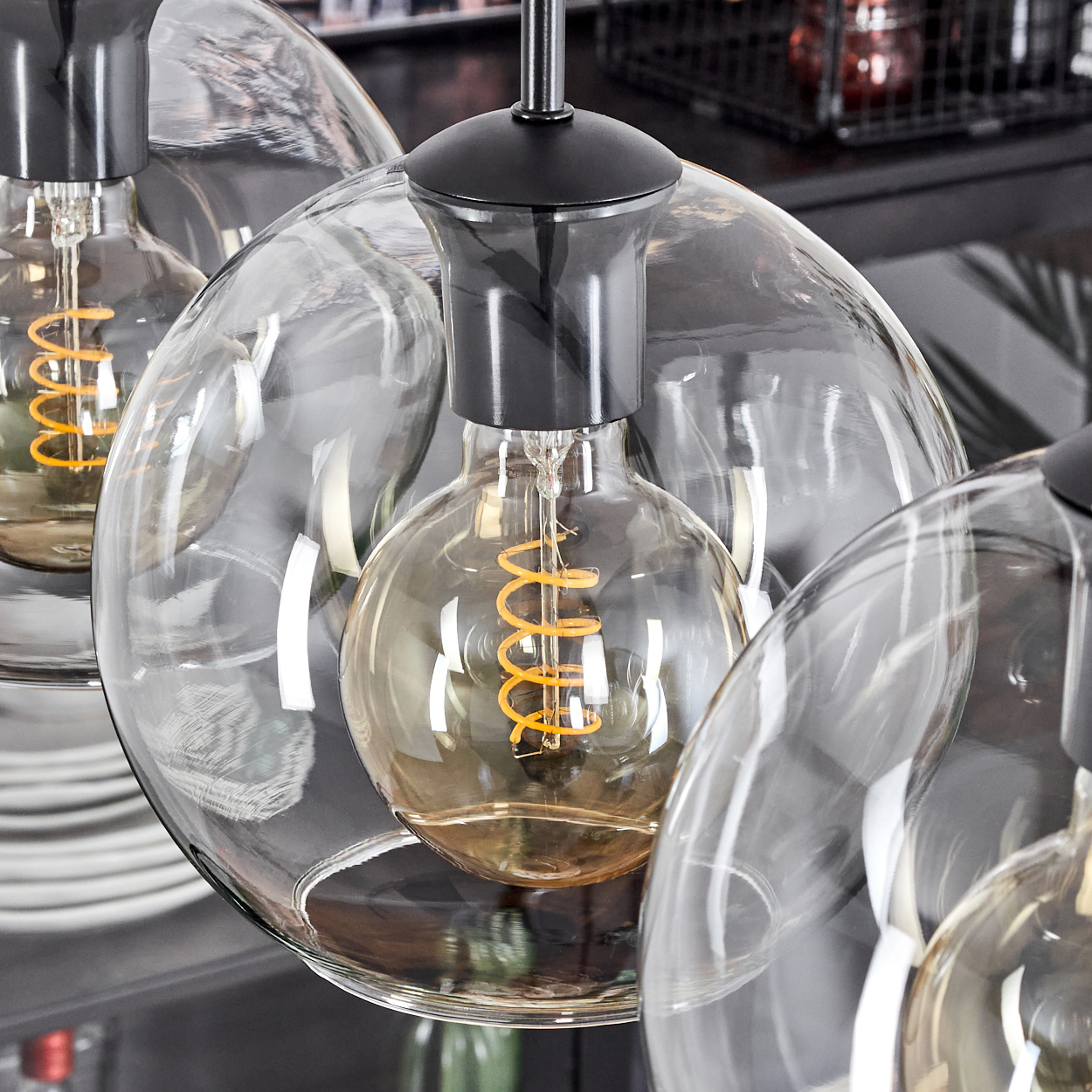 Nahaufnahme von Glas-Pendelleuchten mit Wendelfäden. Schwarze Armaturen und Glasschirme. Hintergrund mit Tellern und Dekoration.