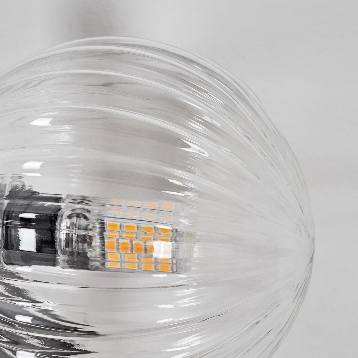 Nahaufnahme einer klaren Glühbirne. Die Birne ist geriffelt und zeigt die inneren Komponenten mit einer gelb-orangen LED.