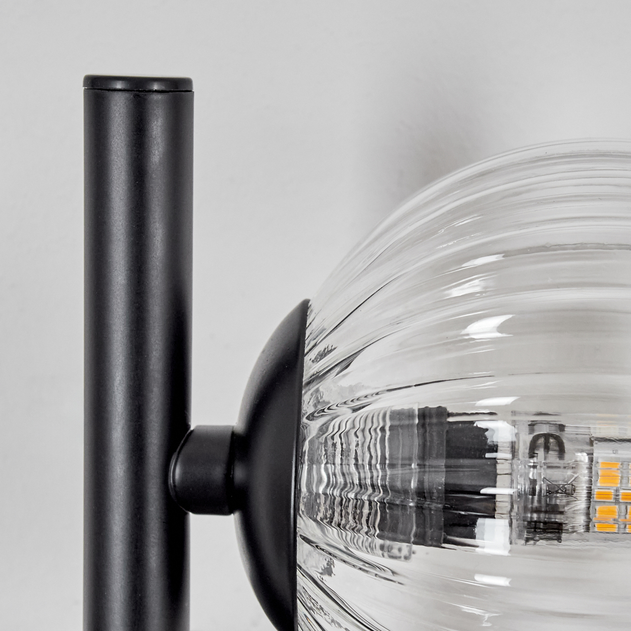 Nahaufnahme einer schwarzen Lampe mit einem klaren, gerippten Glaskolben. Die Lampe befindet sich vor einem weißen Hintergrund. Details der Glühbirne sind sichtbar.