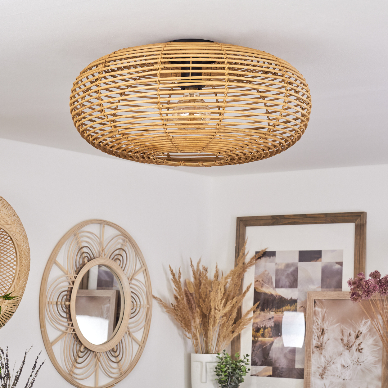 Eine gewebte Rattan-Leuchte hängt von einer weißen Decke. Darunter sind ein Spiegel und gerahmte Kunstwerke sowie dekorative Pflanzen zu sehen.
