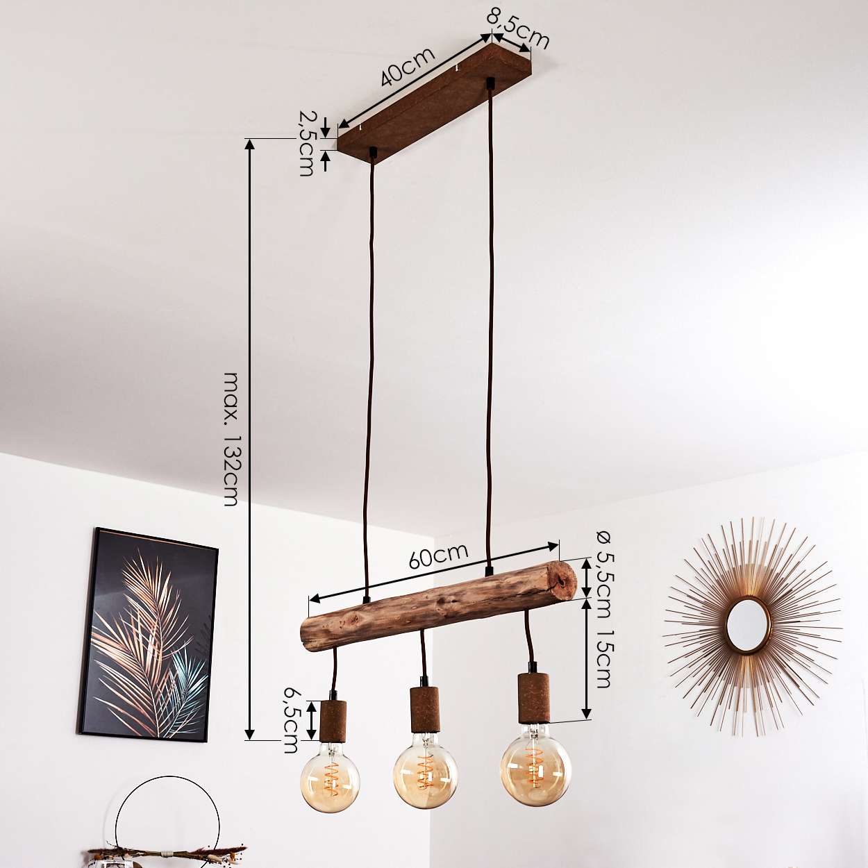 Eine Pendelleuchte aus Holzbalken mit drei Glühbirnen. Maße sind markiert. Ein gerahmtes Bild und ein Sonnenstrahlenspiegel an der weißen Wand.