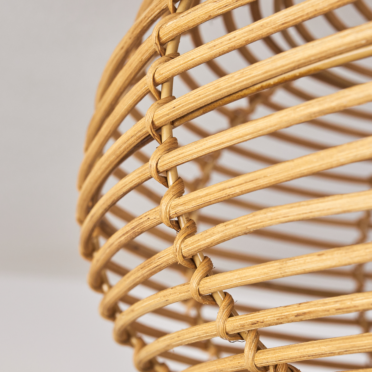 Nahaufnahme eines gewebten Rattan-Lampenschirms. Der hellbraune Schirm besteht aus gebogenen, miteinander verwobenen Streifen, mit weißem Hintergrund.