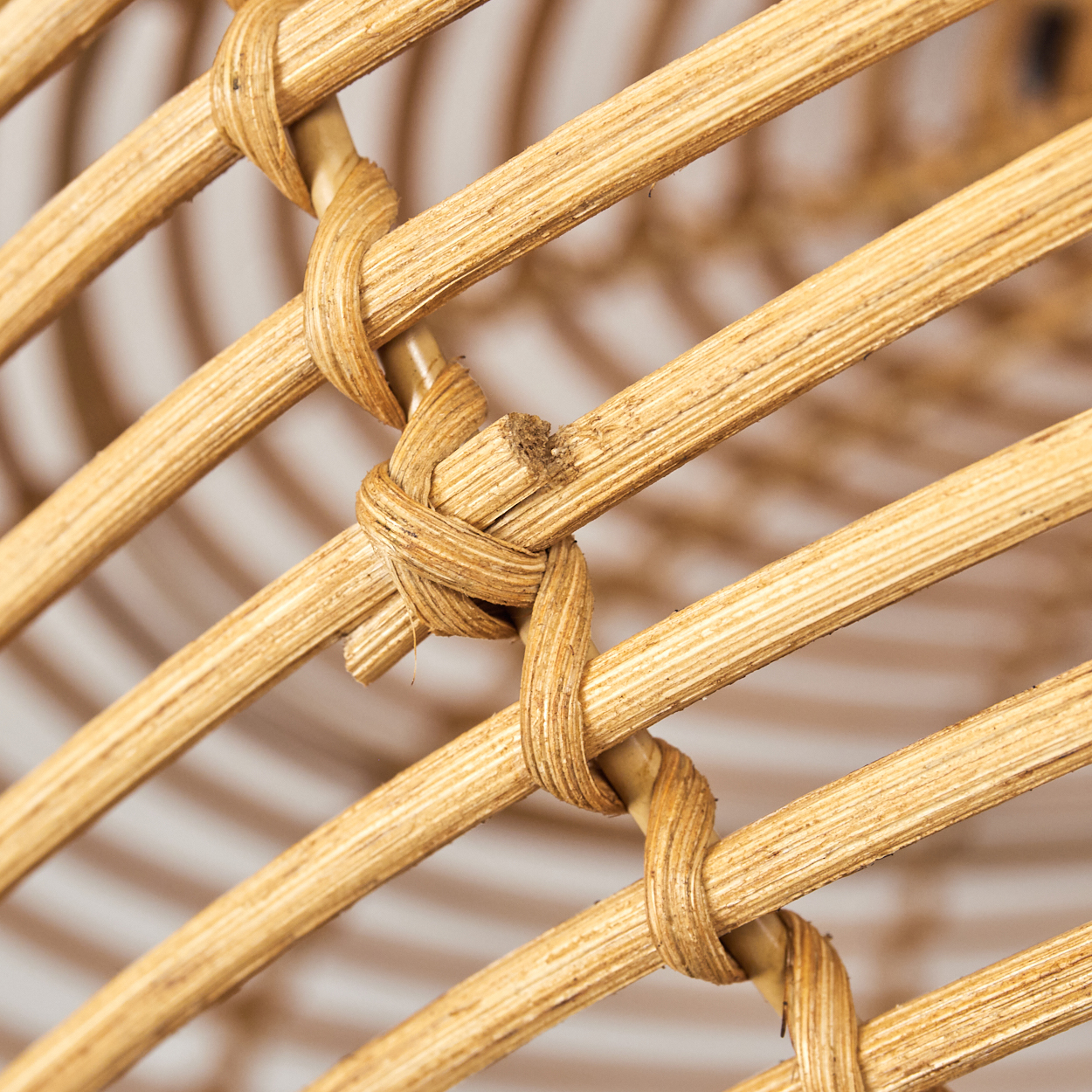 Nahaufnahme von geflochtenem Rattan. Diagonale Stäbe werden durch gewebte Knoten verbunden. Der Hintergrund ist verschwommen und hell.
