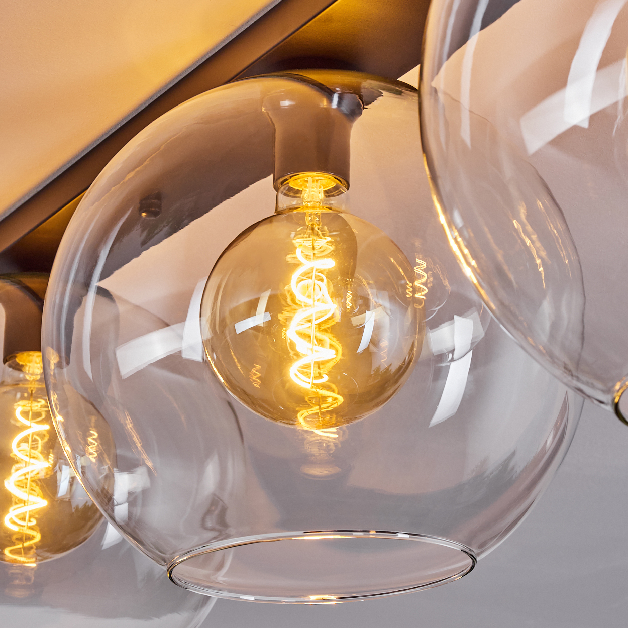 Nahaufnahme einer modernen Leuchte. Klare Glaskugeln umgeben warme, glühende Glühbirnen im Edison-Stil, vor einem dunklen Metallrahmen.