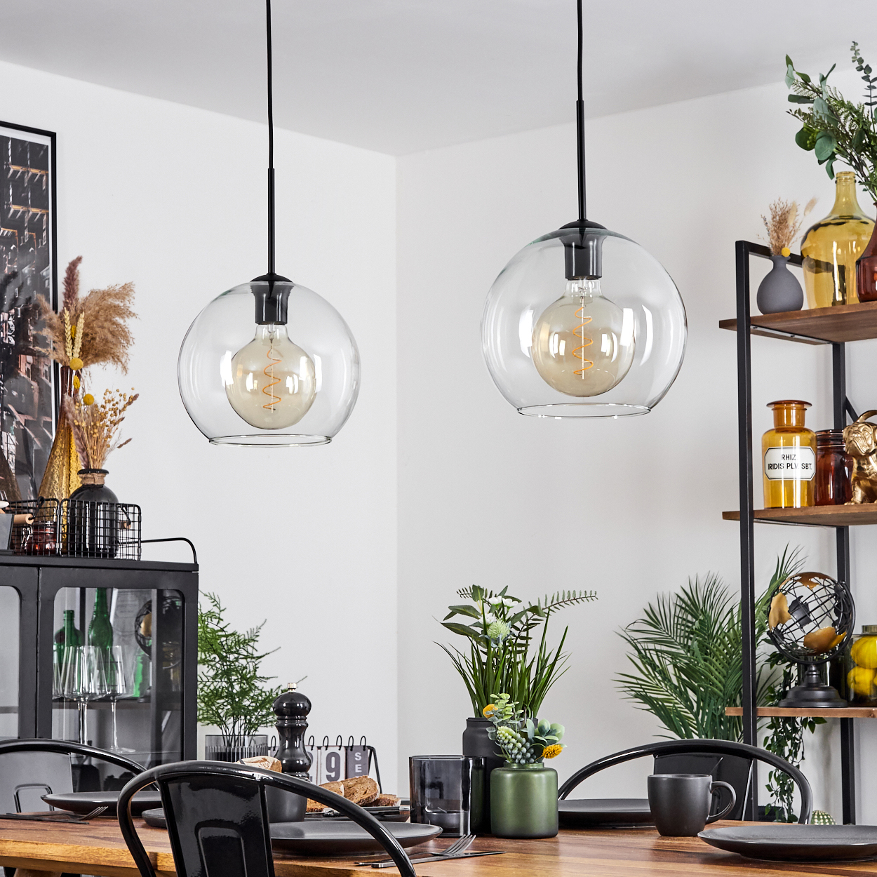 Zwei hängende Glaskugelleuchten beleuchten ein Esszimmer-Set mit Pflanzen und Regalen voller Dekorationen.