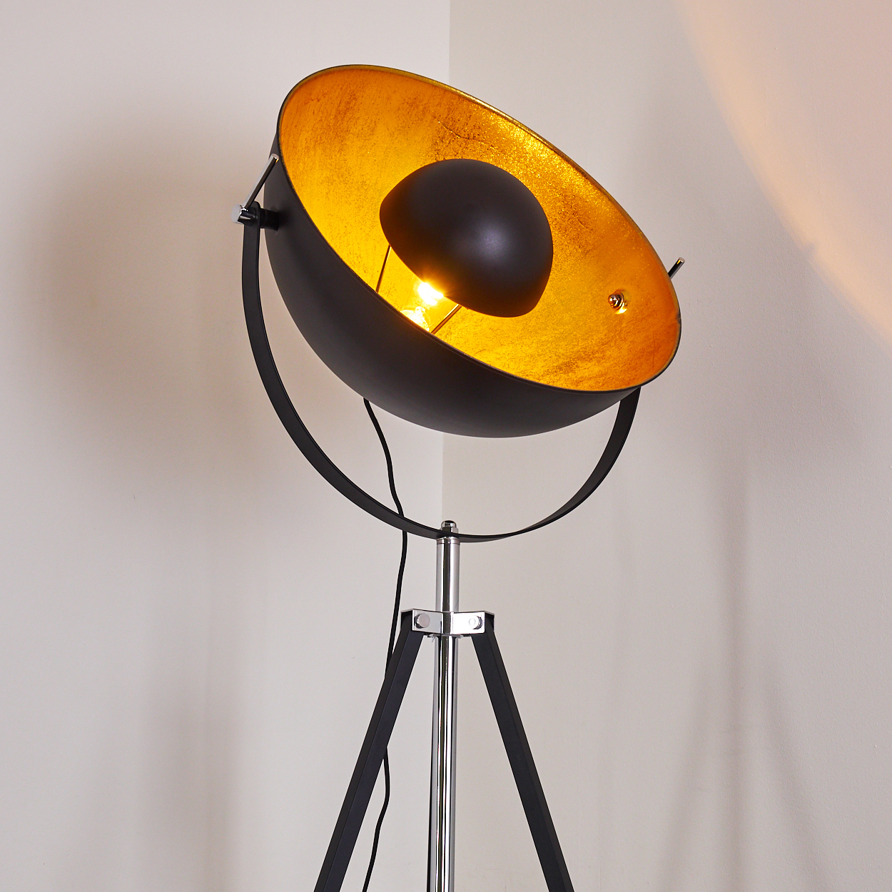 Eine moderne schwarze und goldene Stehlampe steht in einer Ecke. Die Lampe hat ein Stativ und einen großen, schalenförmigen Schirm.