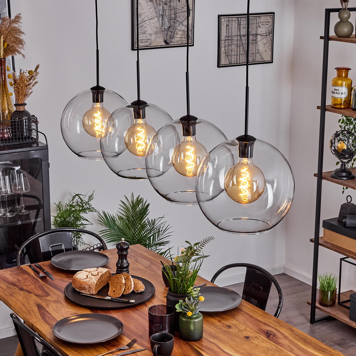 Ein Esszimmer mit einem Holztisch, der für eine Mahlzeit gedeckt ist. Hängende Glaskugelleuchten beleuchten die Szene.