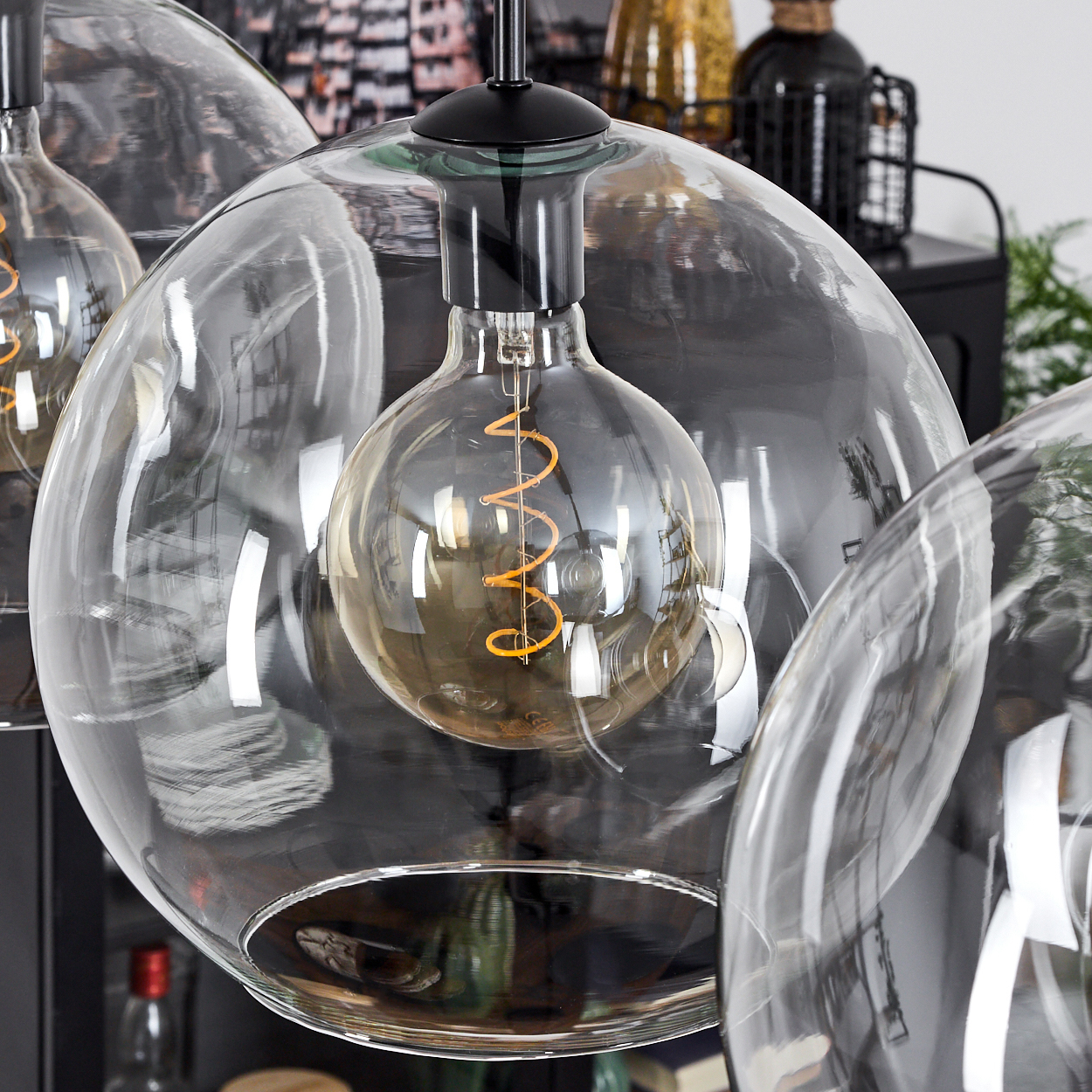 Nahaufnahme einer Glas-Pendelleuchte mit großer Glühbirne und Wendelfaden. Hintergrund zeigt unscharfe Objekte.