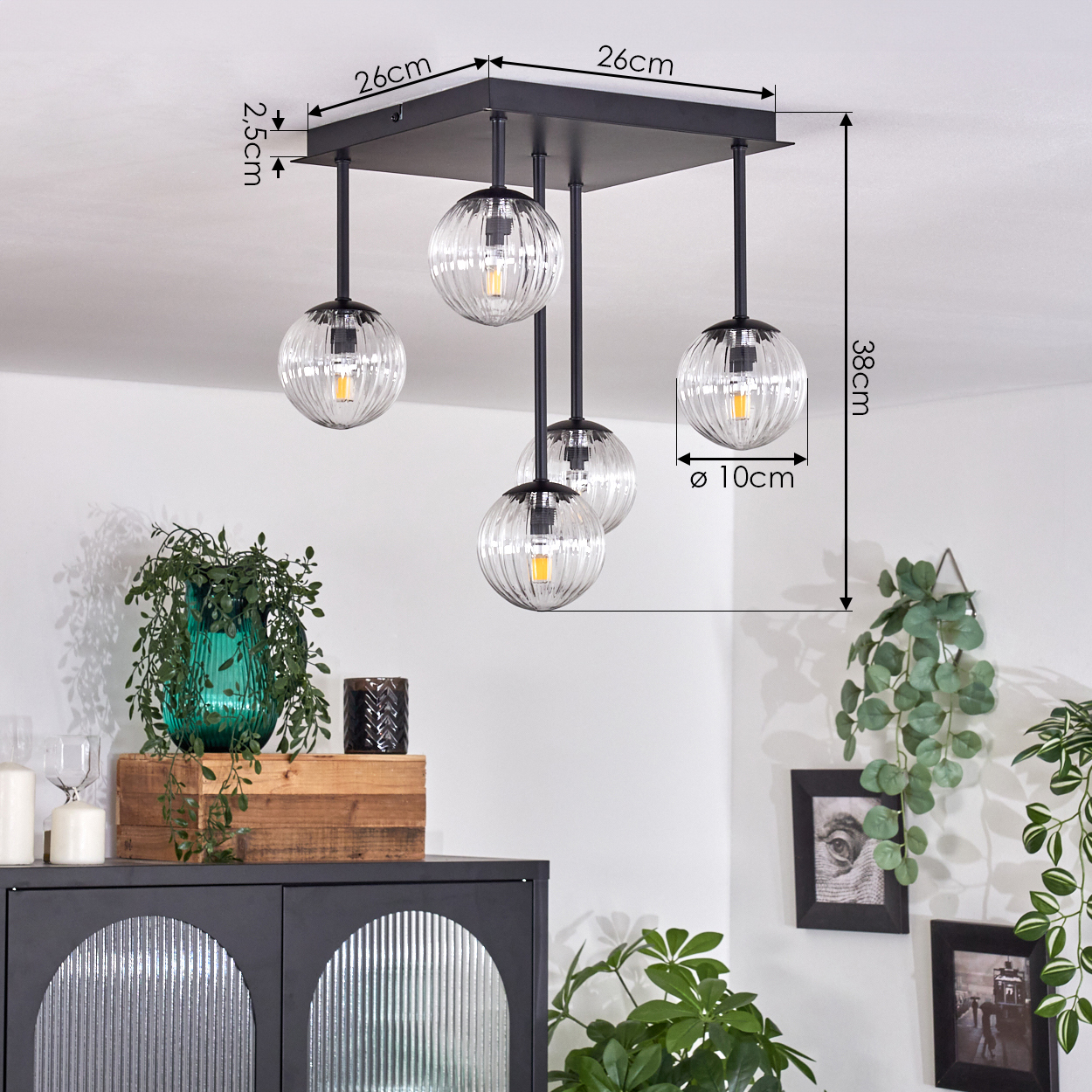 Eine moderne schwarze Deckenlampe mit fünf Glaskugelleuchten. Ein Schrank mit Dekoration und Pflanzen darunter. Maße sind angegeben.