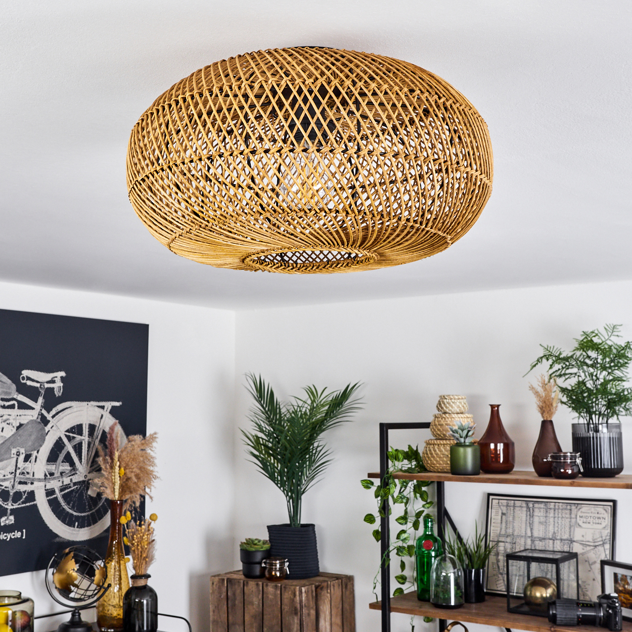 Eine gewebte Rattanlampe hängt an einer weißen Decke. Darunter sind verschiedene Pflanzen, Vasen und Regale angeordnet.