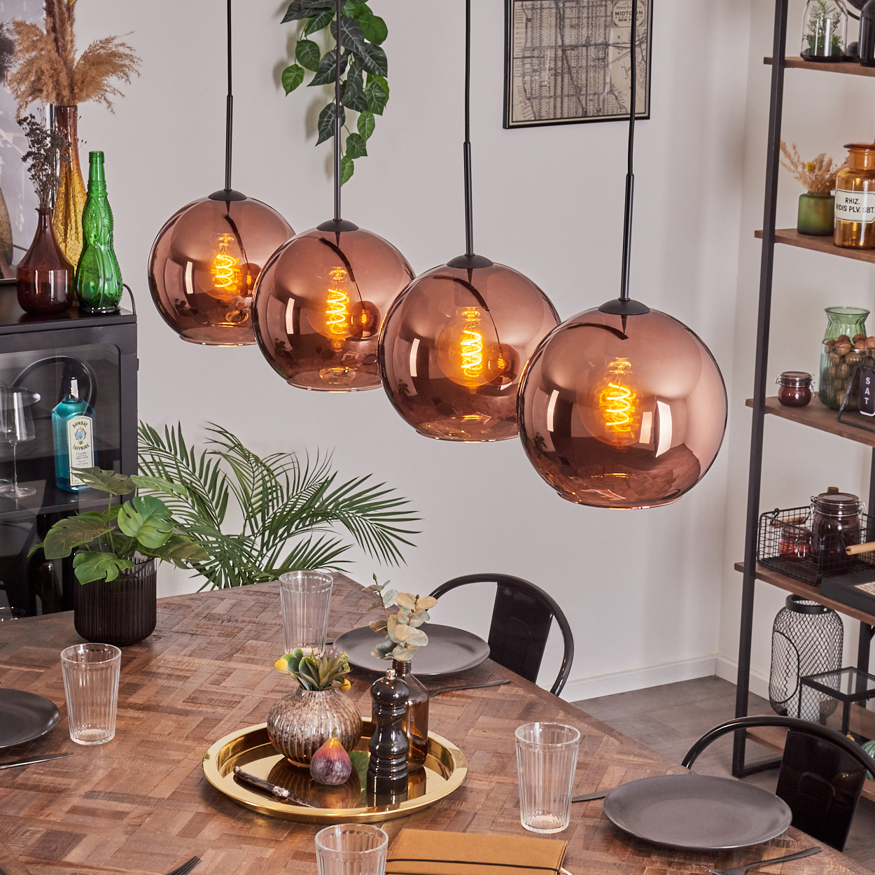 Esszimmer mit kupferfarbenen Pendelleuchten. Holztisch mit Tellern, Gläsern und einer Dekoschale. Regale und Bar im Hintergrund.