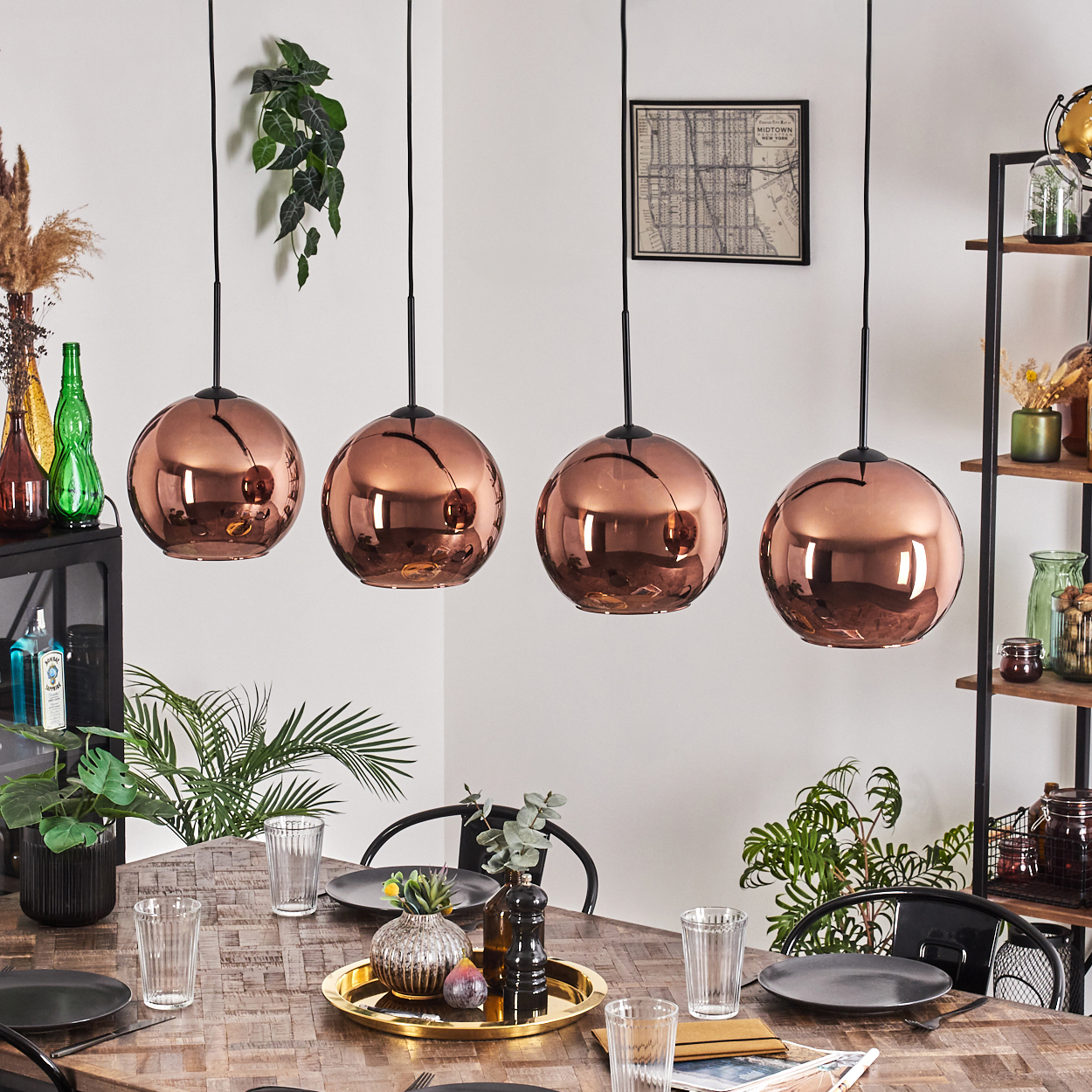 Esszimmer mit kupferfarbenen Pendelleuchten. Holztisch mit Tellern, Gläsern und Dekorationen. Regale mit Gegenständen und Pflanzen.