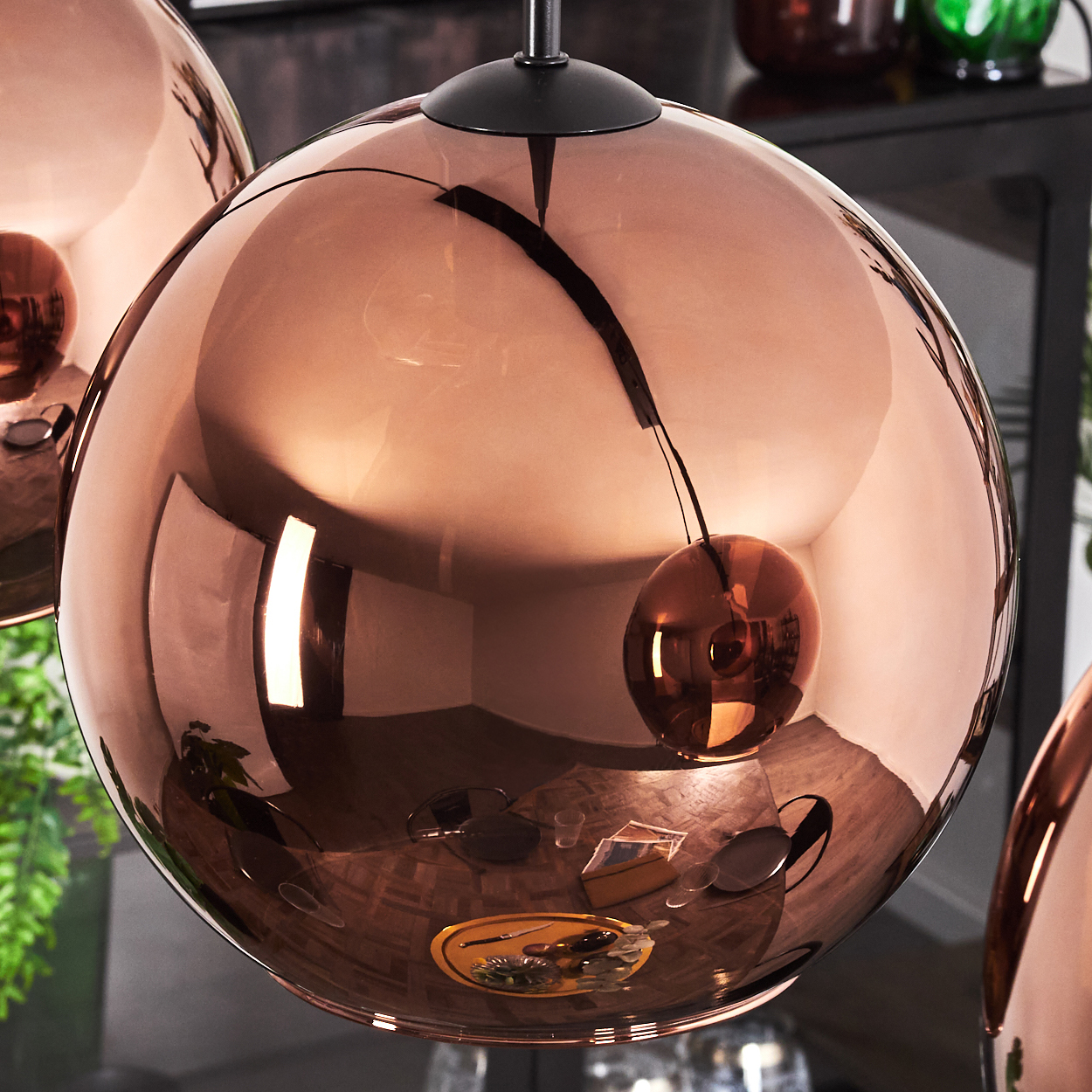 Nahaufnahme einer großen, kupferfarbenen Kugellampe. Sie reflektiert einen Raum mit Holzböden und anderen Objekten.