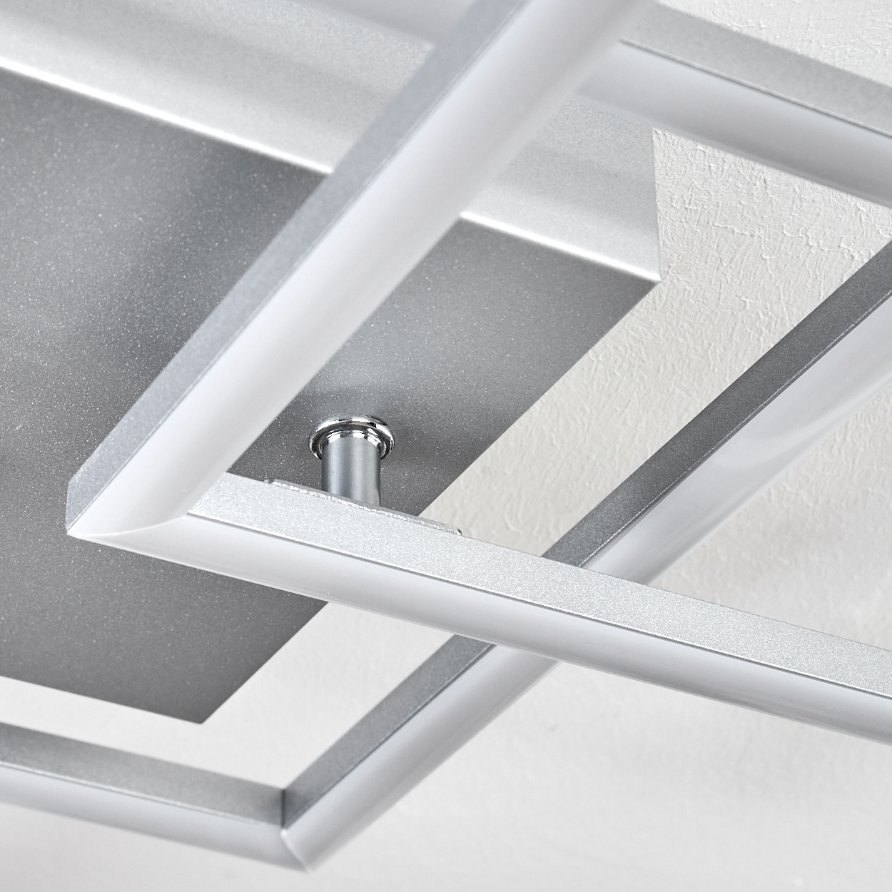 Eine moderne, geometrische Deckenleuchte mit silbernen Rahmen und weißem Licht, montiert an einer strukturierten weißen Decke.