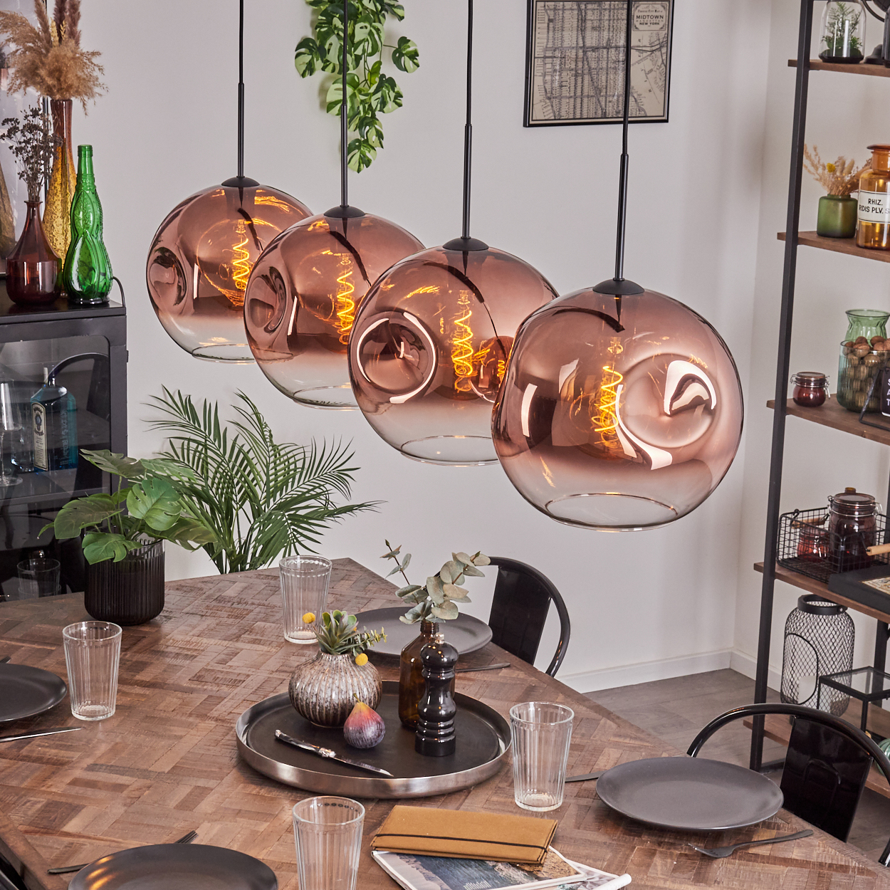 Esszimmer mit Holztisch, vier kupferfarbenen Pendelleuchten und Pflanzen. Tisch gedeckt mit Tellern, Gläsern und Dekoration.