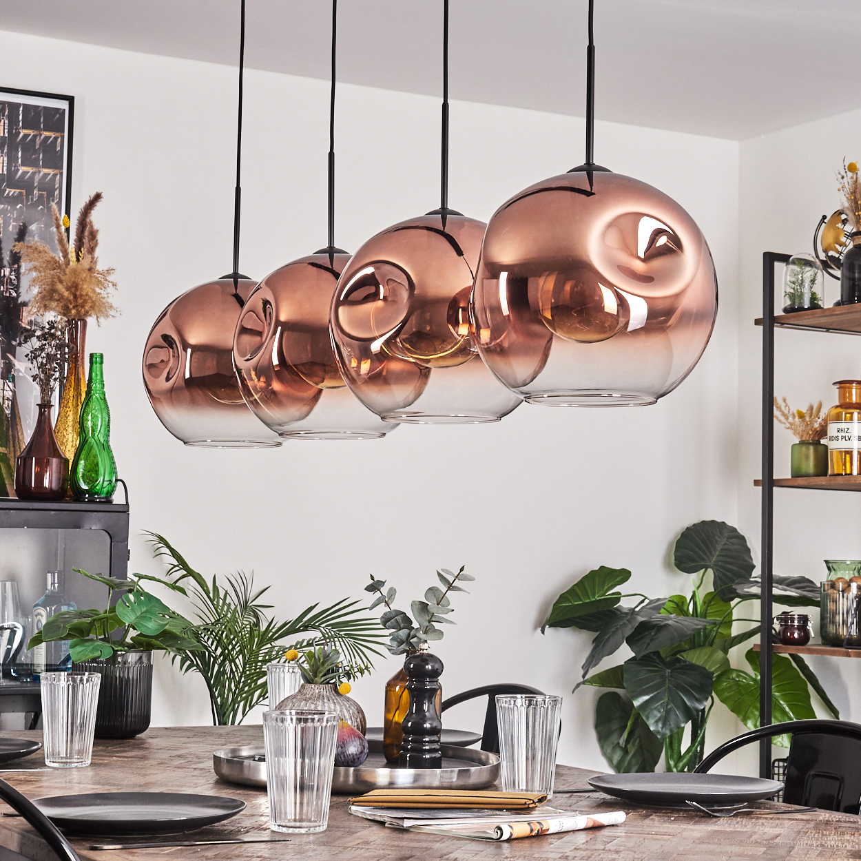 Esszimmer mit kupferfarbenen Hängelampen. Tisch mit Tellern, Gläsern und Pflanzen. Regale mit Dekorationen im Hintergrund.
