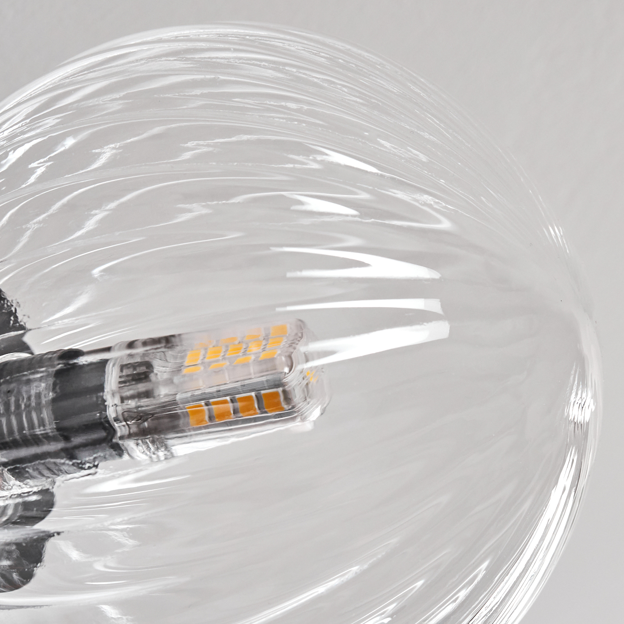 Nahaufnahme einer durchsichtigen, gewirbelten Glasleuchte mit einer kleinen, rechteckigen LED-Glühbirne im Inneren.