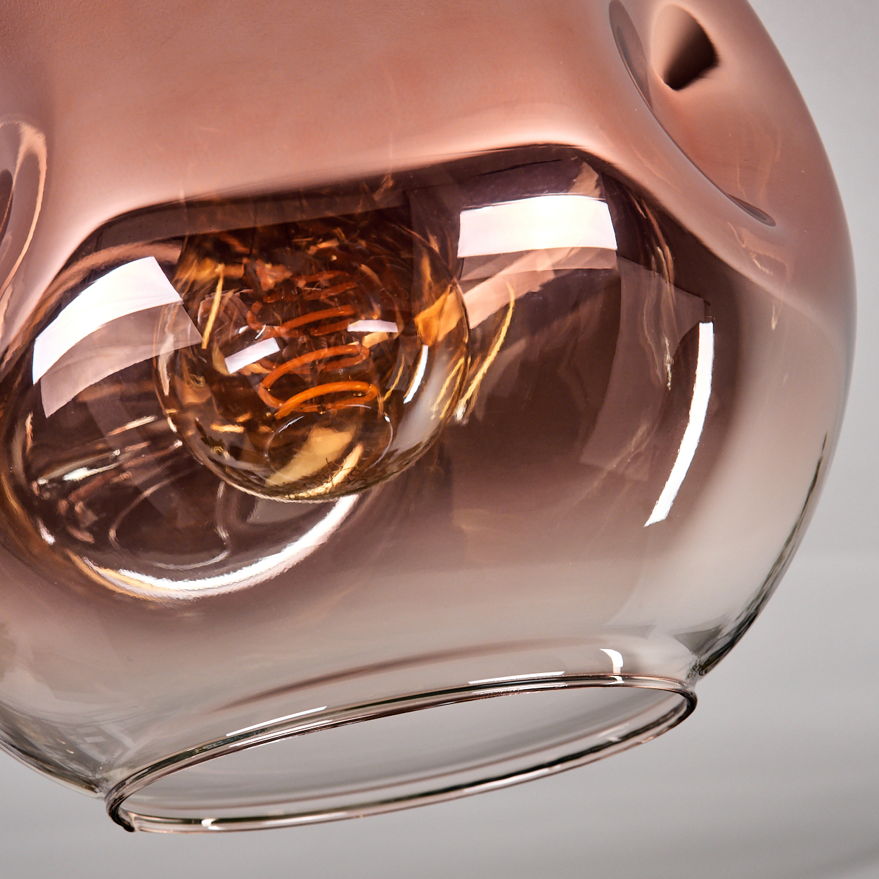 Nahaufnahme einer Glasleuchte mit einer Glühbirne im Inneren. Das Glas hat einen Farbverlauf von Braun und Klar. Der Glühfaden leuchtet.