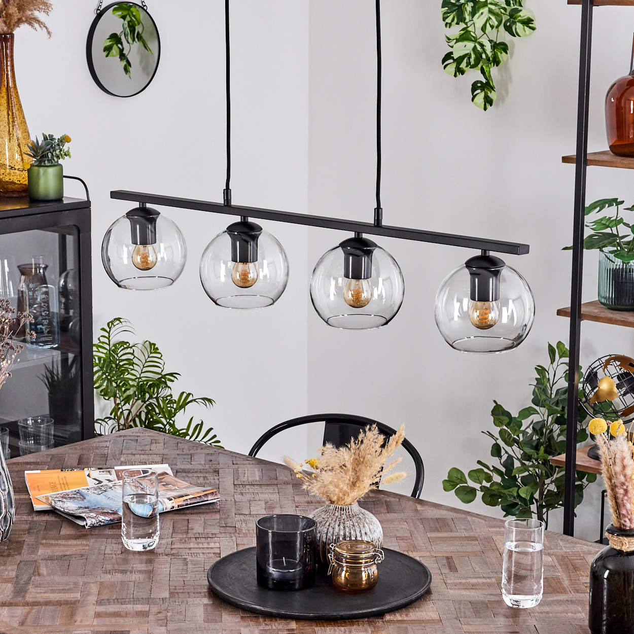 Ein Esszimmer mit Holztisch, schwarzem Kronleuchter mit Glaskugeln. Verschiedene Dekorationen auf dem Tisch und im Hintergrund.