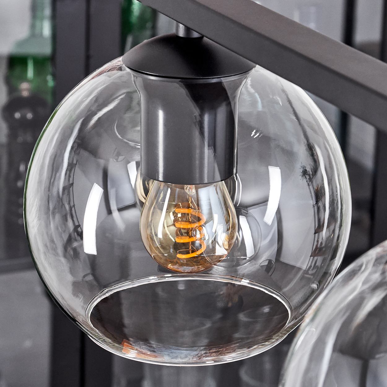 Nahaufnahme einer klaren Glaskugelleuchte. Im Inneren ist eine warm getönte Glühbirne zu sehen. Schwarzes Metall stützt das Glas.