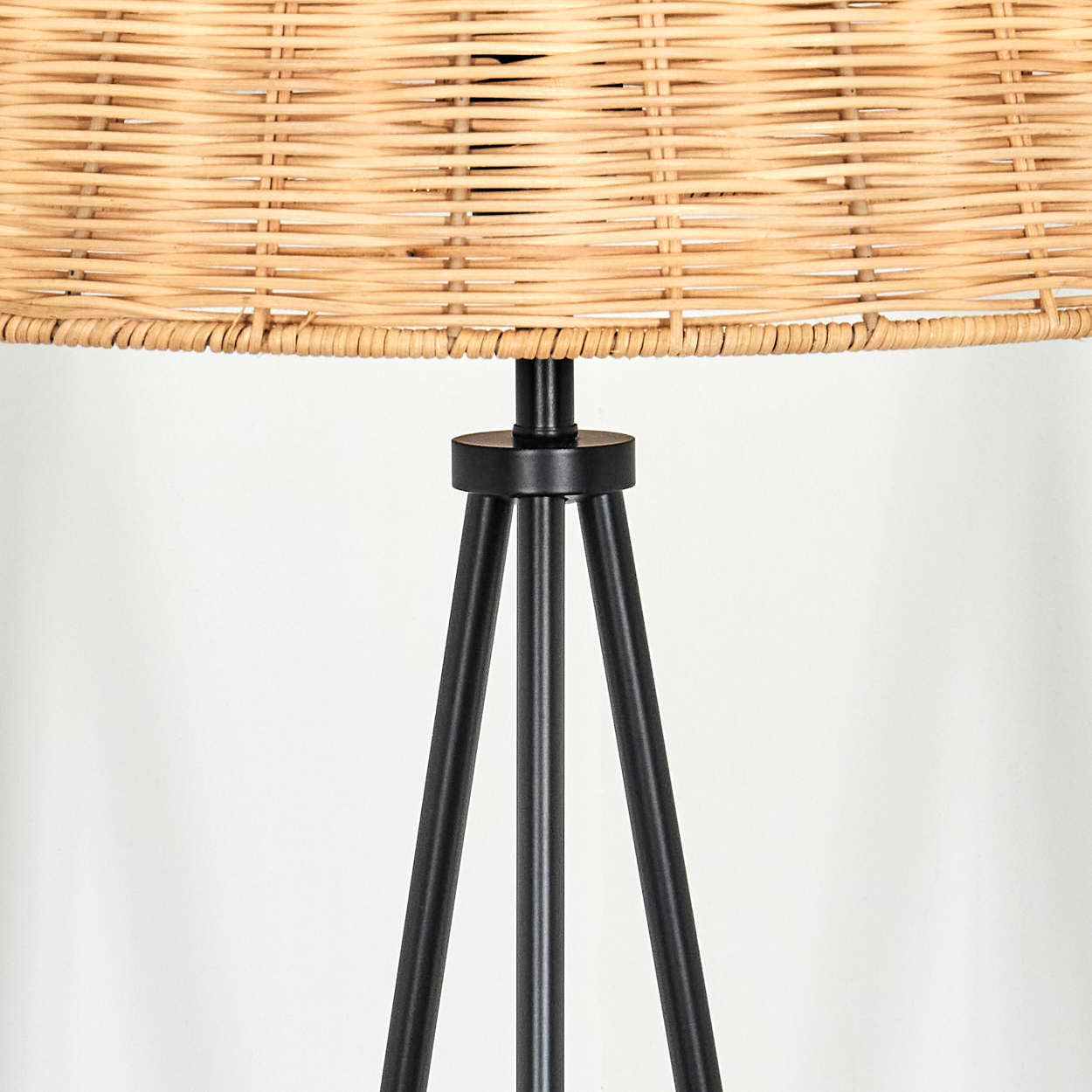 Nahaufnahme einer Lampe. Gewebter beigefarbener Lampenschirm über drei schwarzen Beinen. Weißer Hintergrund.