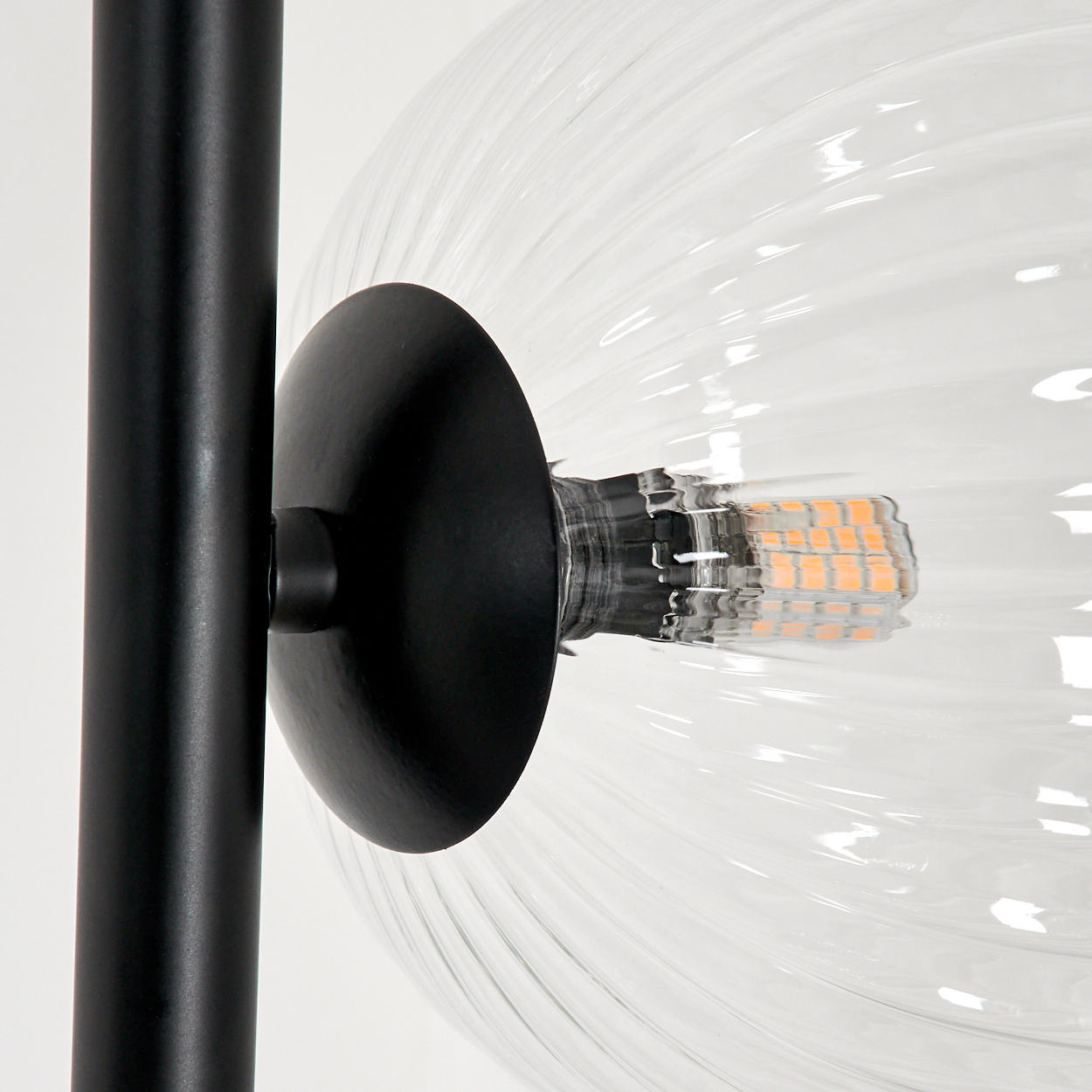 Nahaufnahme einer modernen Lampe. Eine klare Glaskugellampe mit schwarzem Metallsockel und schwarzem Pfosten auf weißem Hintergrund.