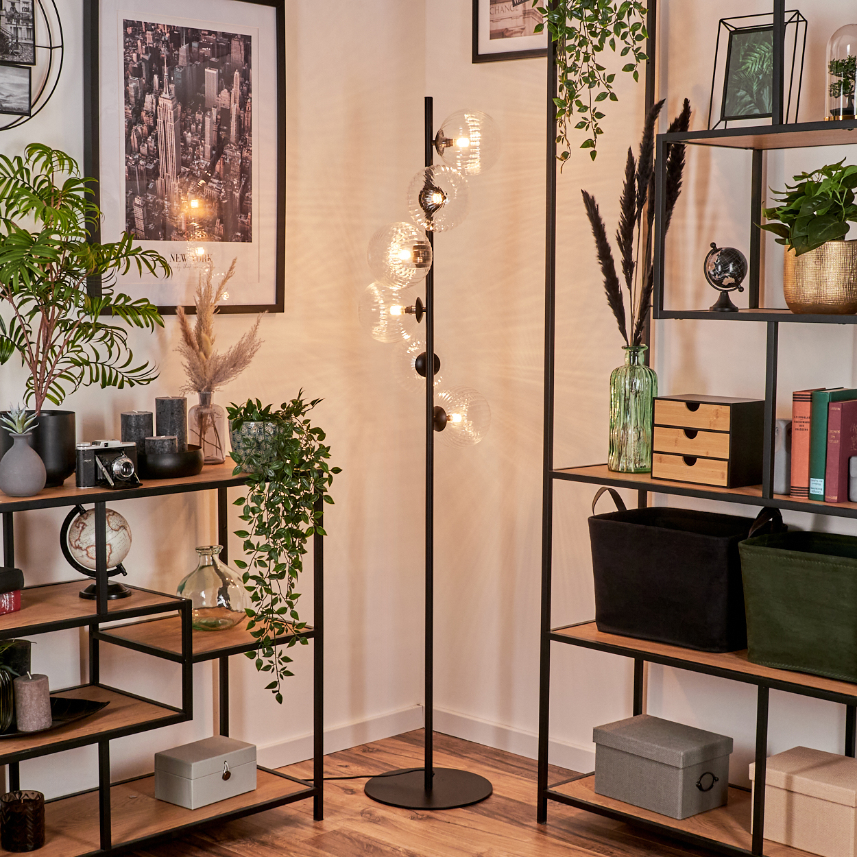 Eine Zimmerecke mit Regalen voller Dekoration, einer Lampe mit Glaskugeln und einem gerahmten New York-Bild. Pflanzen sind zu sehen.
