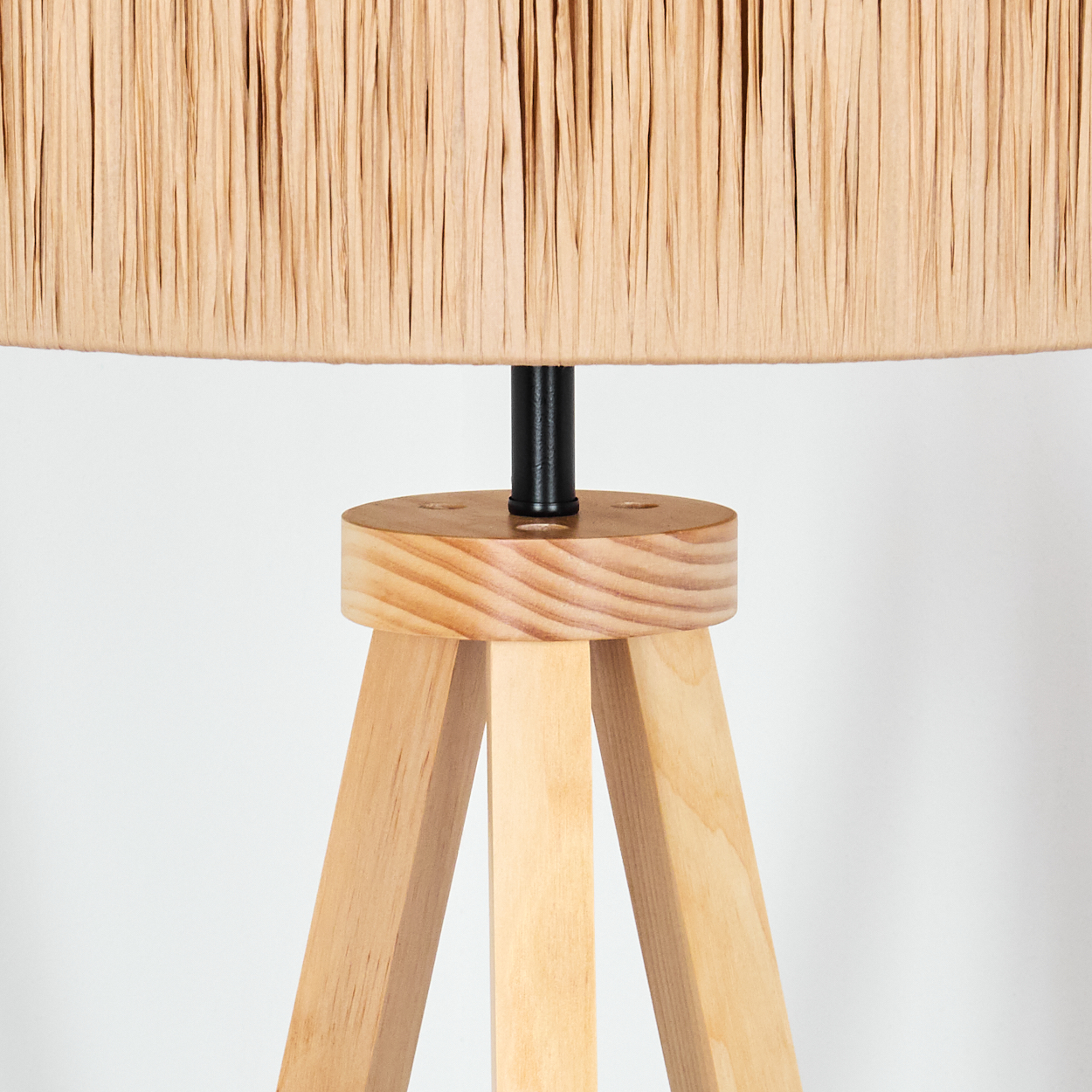 Nahaufnahme einer Lampe. Sie hat einen beigefarbenen Schirm, einen Holzständer und Beine. Der Hintergrund ist weiß.