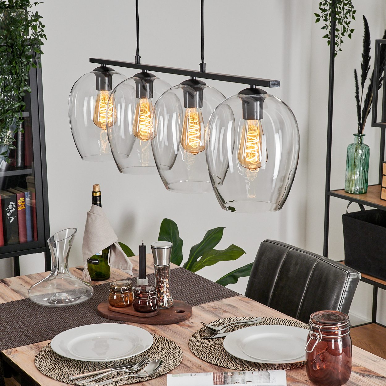 Esszimmer mit Holztisch, gedeckt mit Tellern, Besteck und einem Glas. Überkopf hängen vier Pendelleuchten.