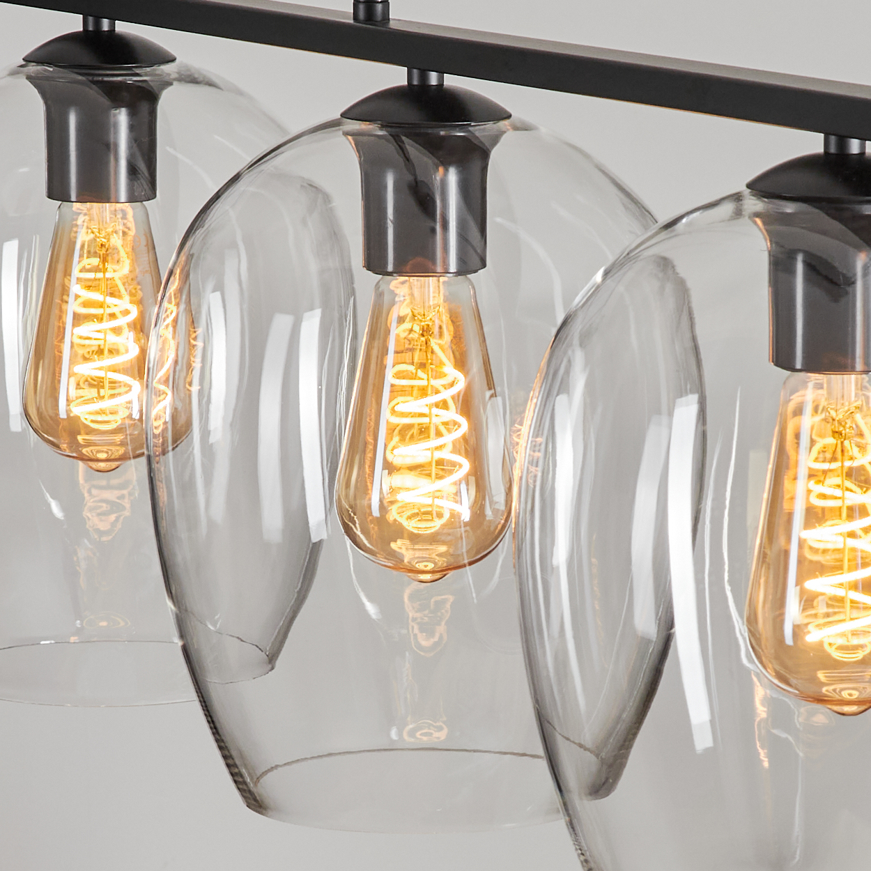 Nahaufnahme einer modernen Leuchte. Drei transparente Glasschirme mit Edison-Glühbirnen. Die Leuchte ist schwarz und auf weißem Grund montiert.