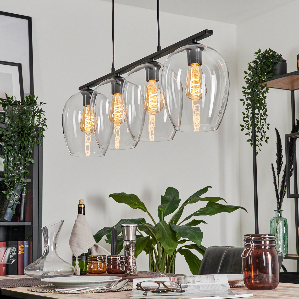 Ein Esstisch mit einer modernen Hängelampe, Pflanzen, Glaswaren und Essaccessoires.