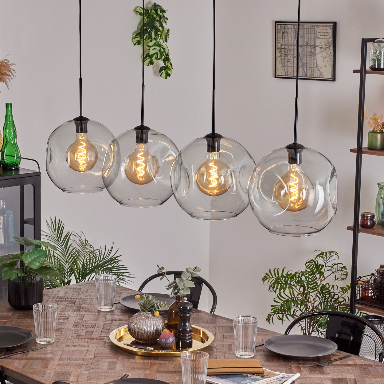 Esszimmer mit Holztisch, vier Globus-Pendelleuchten. Pflanzen, Gläser, Teller und Dekorationsartikel sind auf dem Tisch angeordnet.