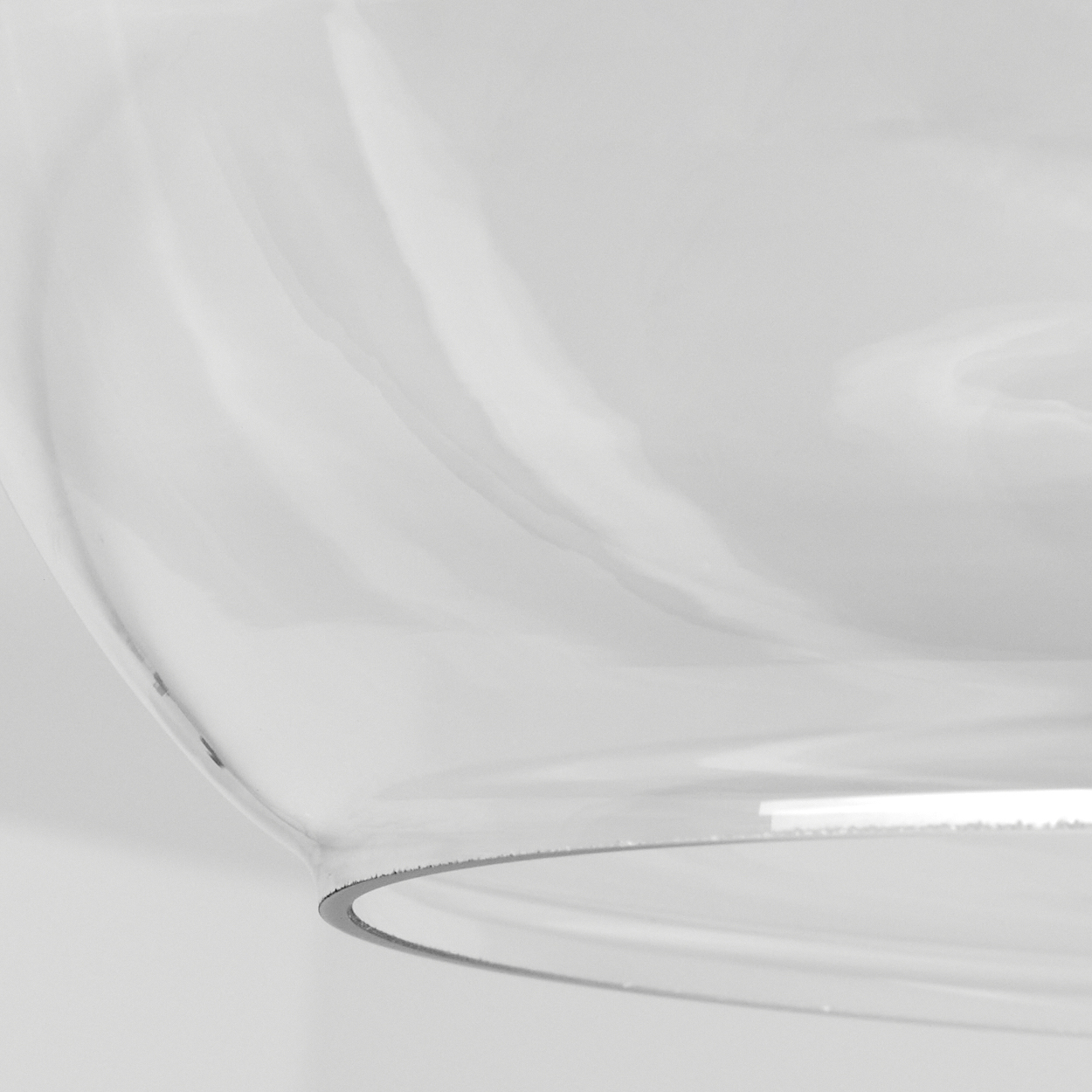 Nahaufnahme eines transparenten Glasobjekts mit gebogenen Kanten vor weißem Hintergrund. Das Glas reflektiert Licht.