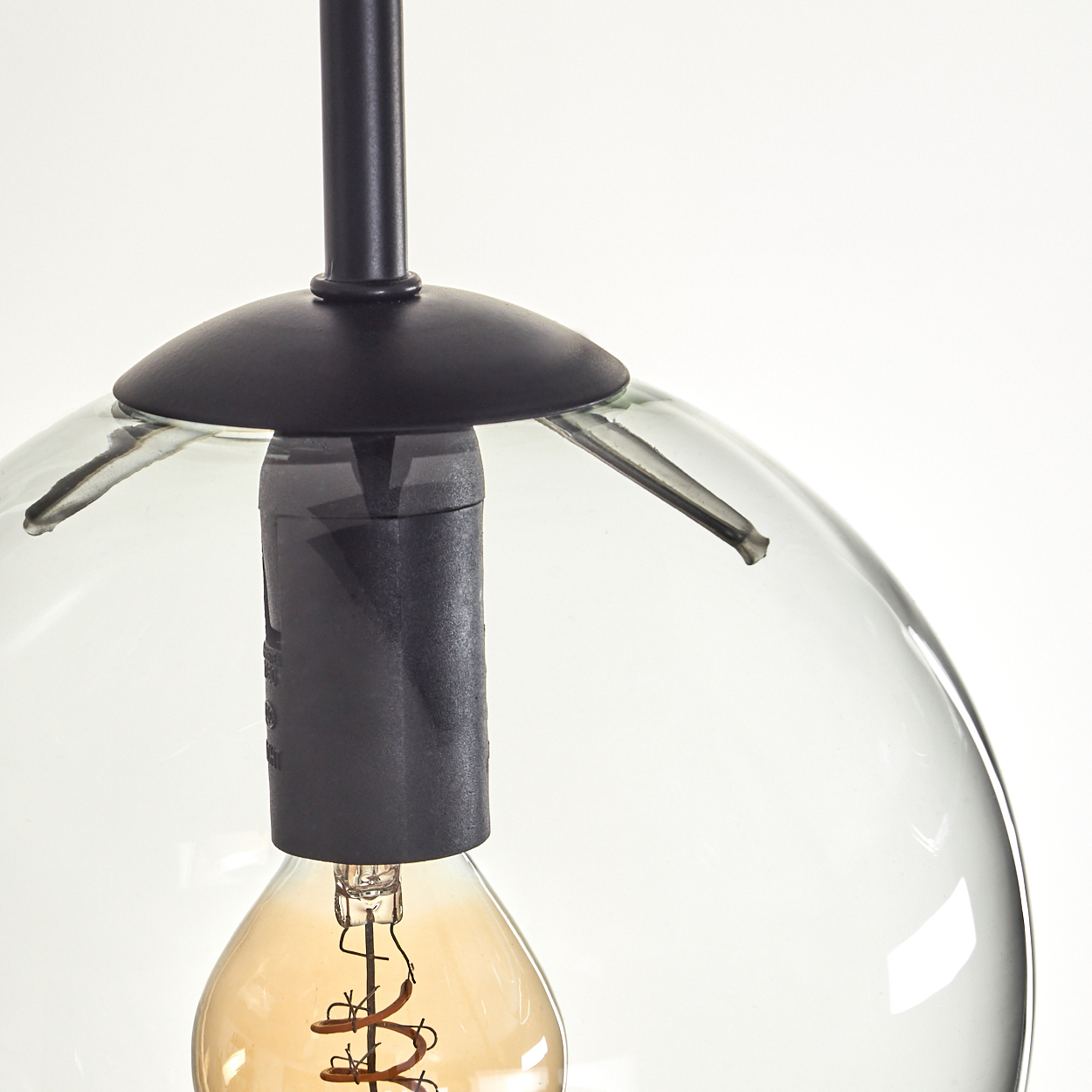 Nahaufnahme einer Pendelleuchte. Sie hat einen klaren Glaskolben, eine schwarze Halterung und eine warmtonige Edison-Glühbirne.